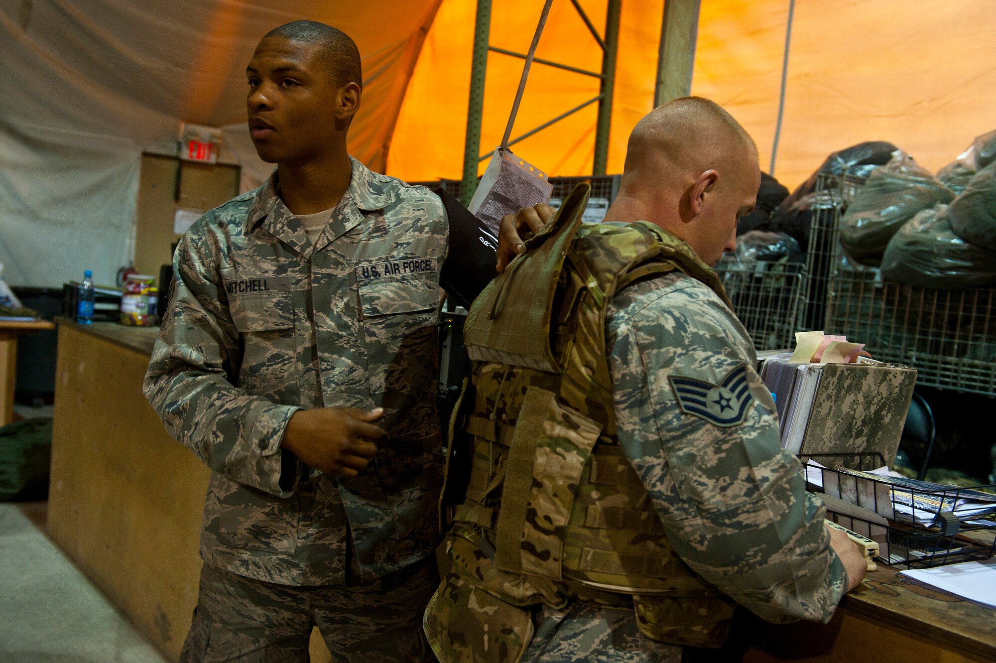 Senior Airman Gregory Mitchell (left) demonstrates how to properly wear individual protective gear to transients with the assistance of Staff Sgt. Seth Tuggle during equipment distribution at the Transit Center at Manas, Kyrgyzstan, August 4, 2012. The Transit Center's Expeditionary Theater Distribution Center equipment technicians assist transients daily on how to properly wear individual protective gear. Both Mitchell and Tuggle are Transit Center ETDC equipment technicians. Mitchell is deployed out of Fairchild Air Force Base, Wash and is a native of Houston. Tuggle is deployed out of Little Rock Air Force Base, Ark. and is a native of Morton, Ill. (U.S. Air Force photo/Senior Airman Brett Clashman)