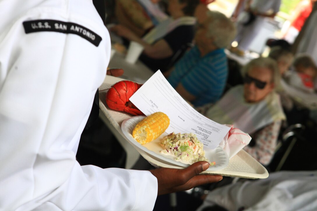 A sailor from the USS San Antonio delivers a freshly cooked lobster to one of the residents at the Knox Center, a nursing facility in Rockland, Maine, during the city’s 2012 Lobster Festival, Aug. 2, 2012. More than 25 Marines and sailors from the San Antonio and Combat Logistics Regiment 27, 2nd Marine Logistics Group visited the facility’s residents during their community engagement activities. (Photo by Lance Cpl. Paul Peterson)