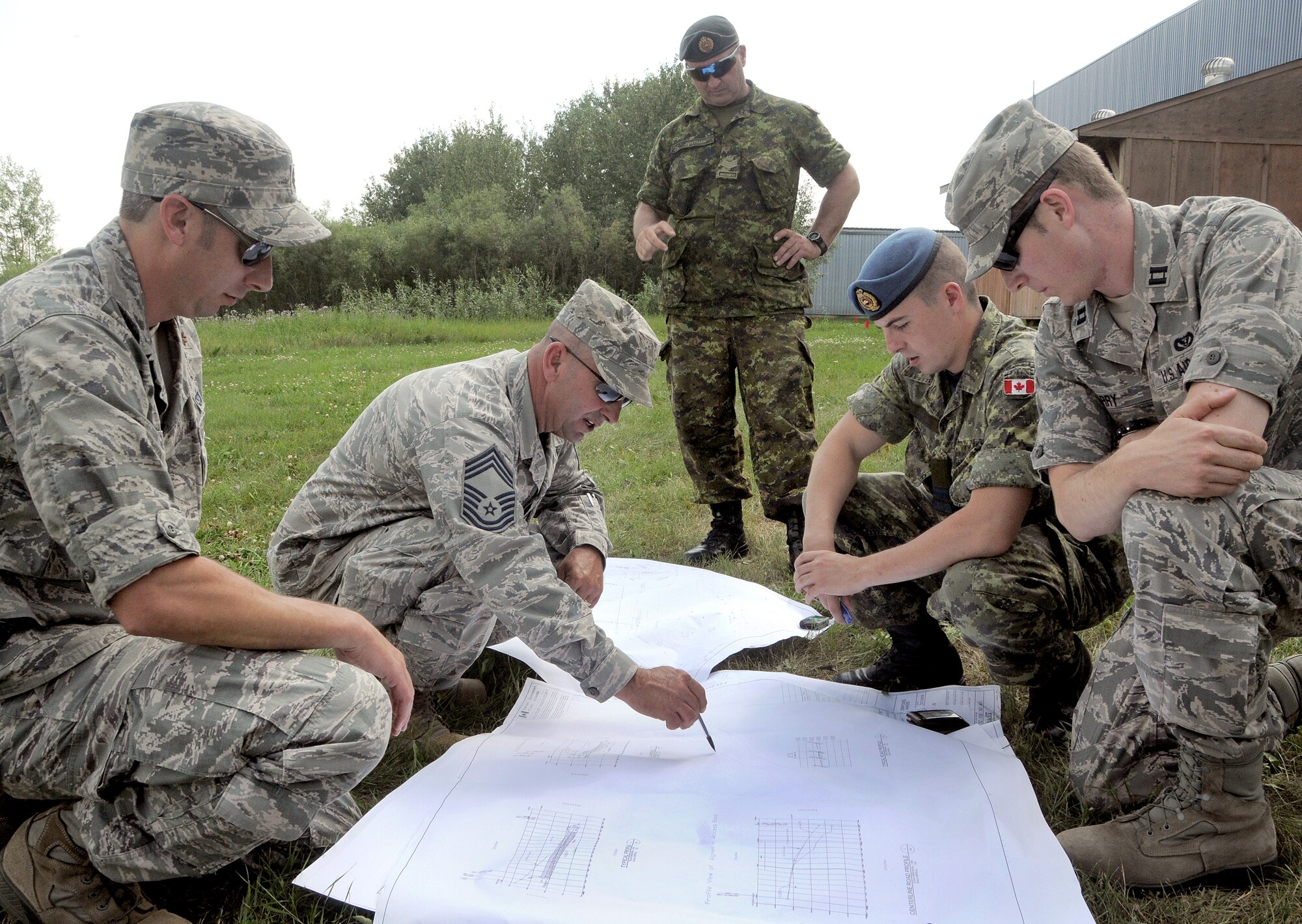 Civil Engineering Squadron team leaders from the 146th Airlift Wing (from left) Maj. Patrick Shanahan, Chief Master Sgt. Kurt Rhame, and Capt. Ryan Barry review plans for the grading project with their Canadian counterparts Sgt.  Shaughn Wittman (standing) and Lt. Nicholas Claveau from 4 Wing, Canadian Forces.  The 146th Airlift Wing CES, Channel Islands Air National Guard Station, Port Hueneme, Calif. performed their annual training at Canadian Forces Base, Cold Lake, Alberta, Canada July 28-Aug. 11, 2012. The Civil Engineers took on several ventures, including a renovation at a children’s day care center and a grading project for a concrete storage compound to support sea containers. (U.S. Air Force photo by Tech. Sgt. Alex Koenig)