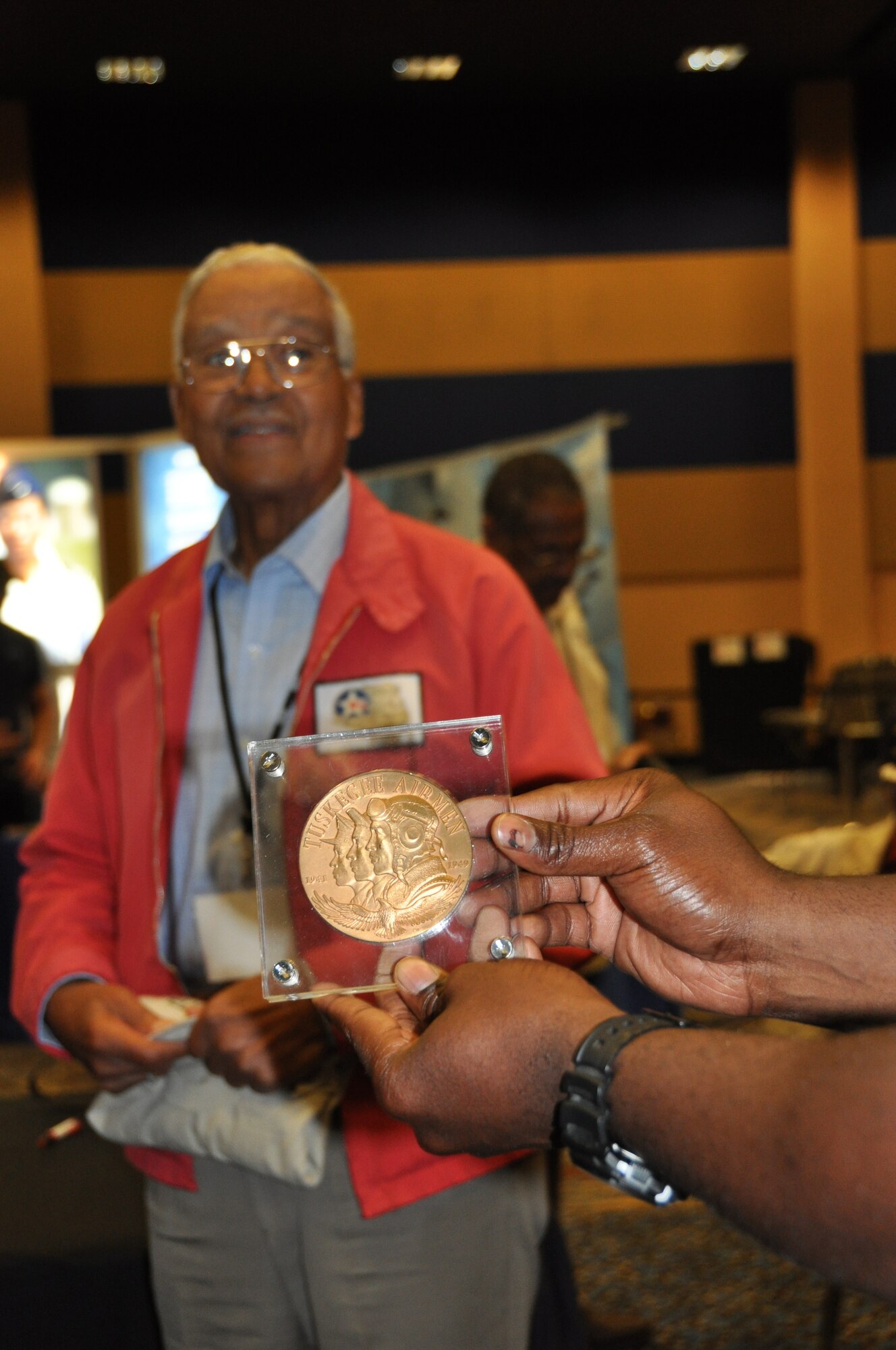 Senior Airman Marren Clay, 477th Aircraft Maintenance Squadron crew chief, holds Tuskegee Airman Col. (Ret.) Charles McGee’s Congressional Gold Medal. McGee, in the background, donated his medal for display in the 302nd Fighter Squadron. McGee along with other Tuskegee Airmen were presented the medal in 2007 by President George W. Bush for their long-ago heroism. Individual Airmen received bronze replicas while the original gold medal resides at the Smithsonian Institution in Washington D.C. (U.S. Air Force photo/Capt. Ashley Conner) 