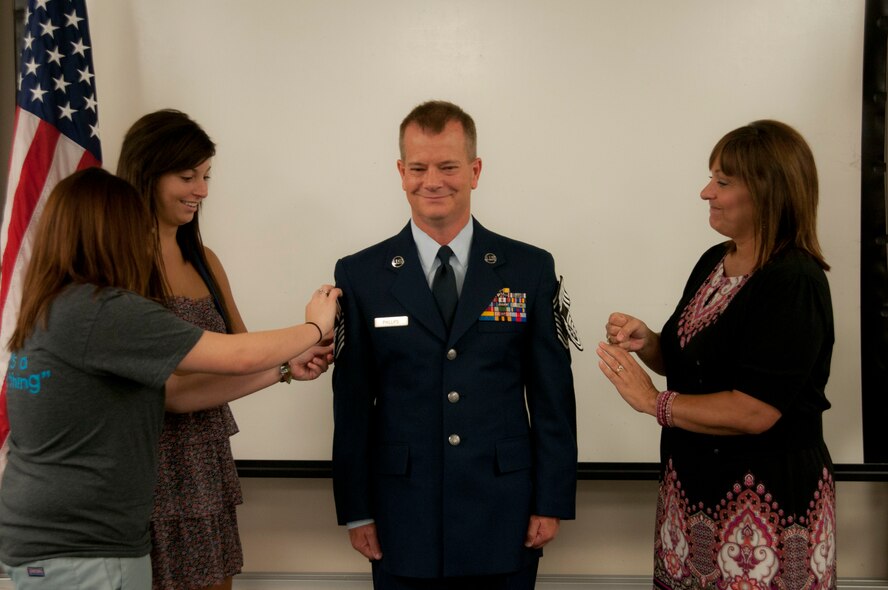 Chief Master Sgt. Craig Phillips has his new rank stuck onto his Air Force dress uniform by his wife and daughters during a promotion ceremony August 3, 2012 at Rosecrans Air National Guard Base, Missouri National Guard. Phillips is the Airfield Operations Manager for the base’s 139th Airlift Wing. (U.S. Air Force photo/Senior Airman Katie Kidd) 