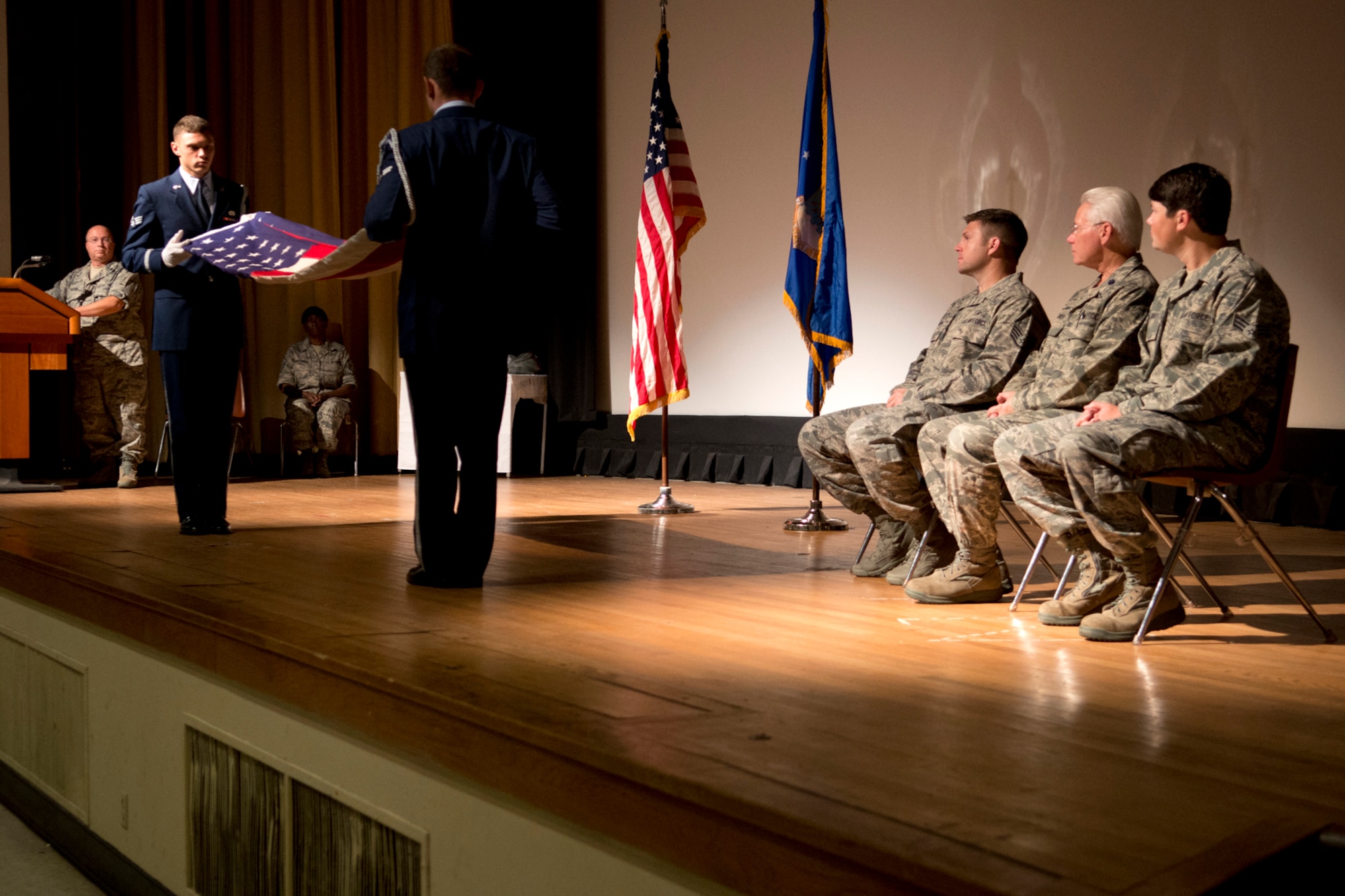 Members of the Barksdale Air Force Base Honor Guard fold an American Flag before presenting it to U.S. Air Force Lt. Col. Allen Smith during a retirement ceremony on Aug. 5, 2012, Barksdale AFB, La. Smith (center) is joined onstage by his two sons, Staff Sgt. Patrick Smith and Senior Airman Eric Smith. (U.S. Air Force photo by Master Sgt. Greg Steele/Released)