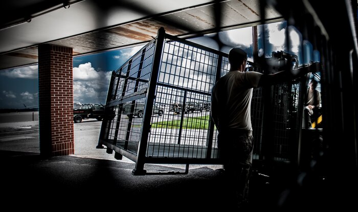 Airman 1st Class Trevor Vascellaro, 437th Aerial Port Squadron passenger service agent, moves a steel baggage bin to the flightline for loading bags onto an aircraft, while Airman 1st Class George Garner, 437th APS passenger service agent, guides him away from the building Aug. 6, 2012 at Joint Base Charleston – Air Base, S.C. The 437th APS baggage claim service team recently upgraded their baggage bins from weathered wooden bins to steel bins for transporting military member’s baggage from and to aircraft. (U.S. Air Force photo by Senior Airman Dennis Sloan)
