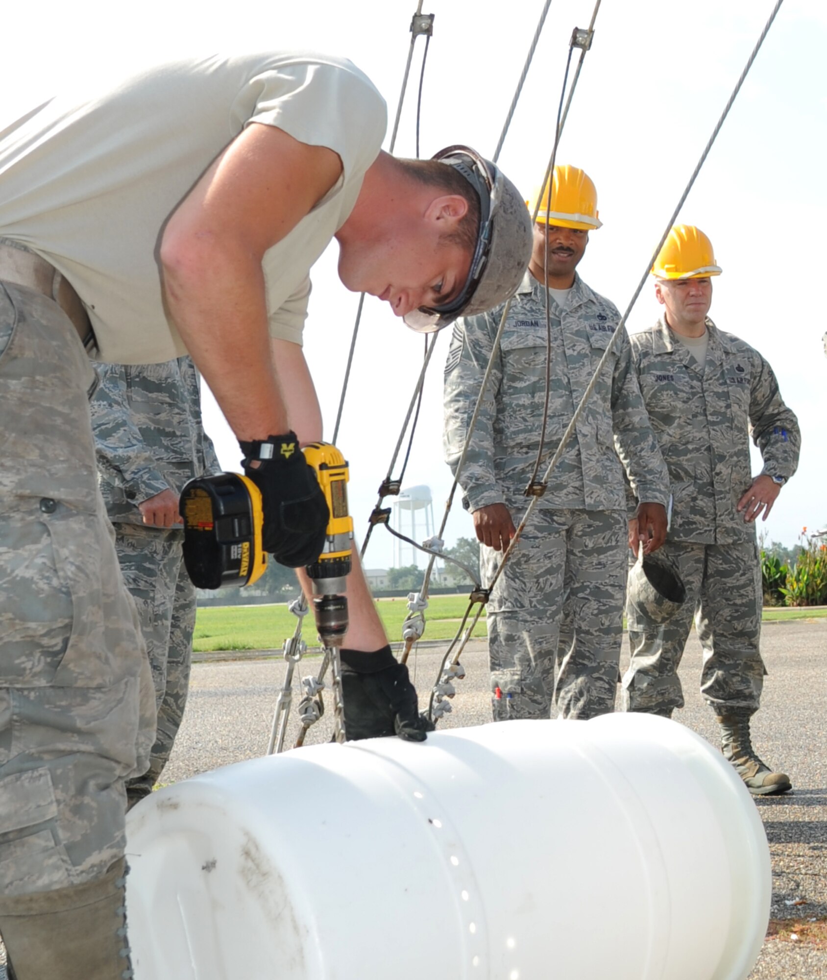 Airman 1st Class Joshua Bogenrief, 85th Engineering Installation Squadron, drills holes in a plastic barrel to be used in an underground trench, while Chief Master Sgts. Linus Jordan, Air Force Space Command command chief, Peterson Air Force Base, Colo., and William Jones, 688th Information Operations Wing command chief, Lackland Air Force Base, Texas, observe the progress of the communications project August 9, 2012, at Keesler Air Force Base, Miss.  The two chiefs along with Chief Master Sgt. Alfred Herring, 24th Air Force command chief, Lackland AFB, Texas, visited the 85th EIS for a one-day visit of its facilities and current projects and conducted enlisted calls.  (U.S. Air Force photo by Kemberly Groue)