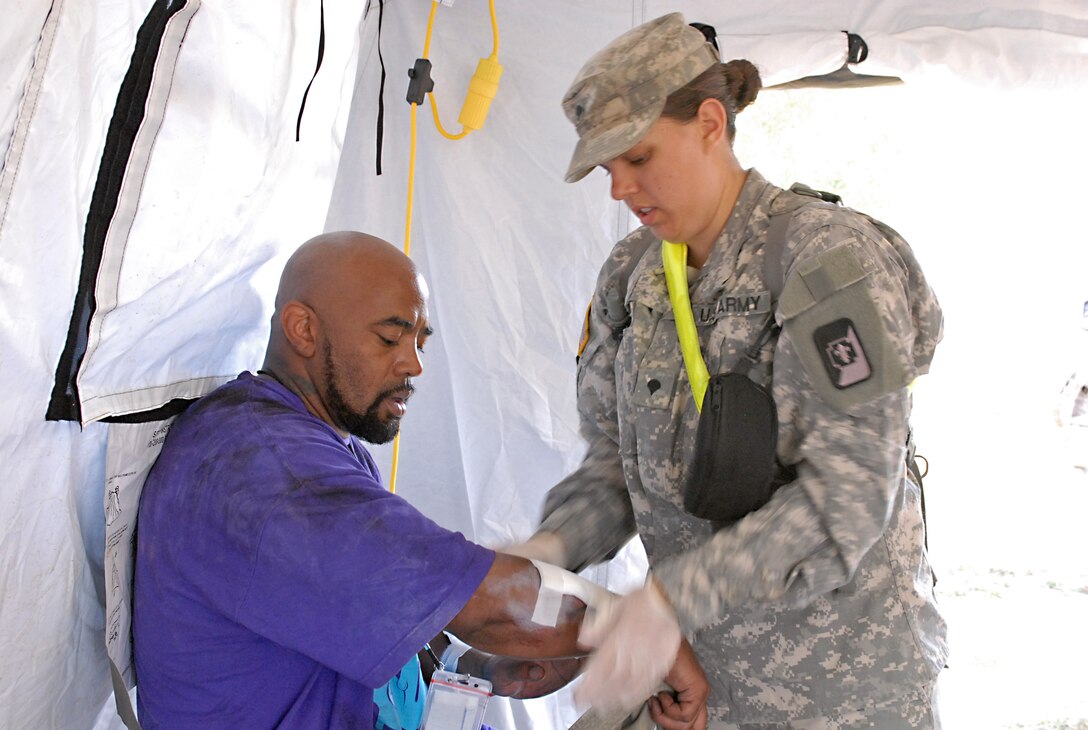 U.S. Army Spc. Sarah Hull, a combat medic assigned to the 547th Area Support Medical Company, 56th Multifunctional Medical Battalion, 62nd Medical Brigade out of Joint Base Lewis-McChord, Wash., bandages a simulated displaced citizen, during a Vibrant Response 13 field-training exercise at the Muscatatuck Urban Training Center, Ind., July 26.  Hull and other combat medics on the scene worked quickly to treat more than 100 survivors in need of medical care. (US Army photo by Sgt. Terence Ewings/ Released)