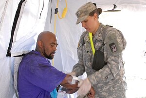 U.S. Army Spc. Sarah Hull, a combat medic assigned to the 547th Area Support Medical Company, 56th Multifunctional Medical Battalion, 62nd Medical Brigade out of Joint Base Lewis-McChord, Wash., bandages a simulated displaced citizen, during a Vibrant Response 13 field-training exercise at the Muscatatuck Urban Training Center, Ind., July 26.  Hull and other combat medics on the scene worked quickly to treat more than 100 survivors in need of medical care. (US Army photo by Sgt. Terence Ewings/ Released)