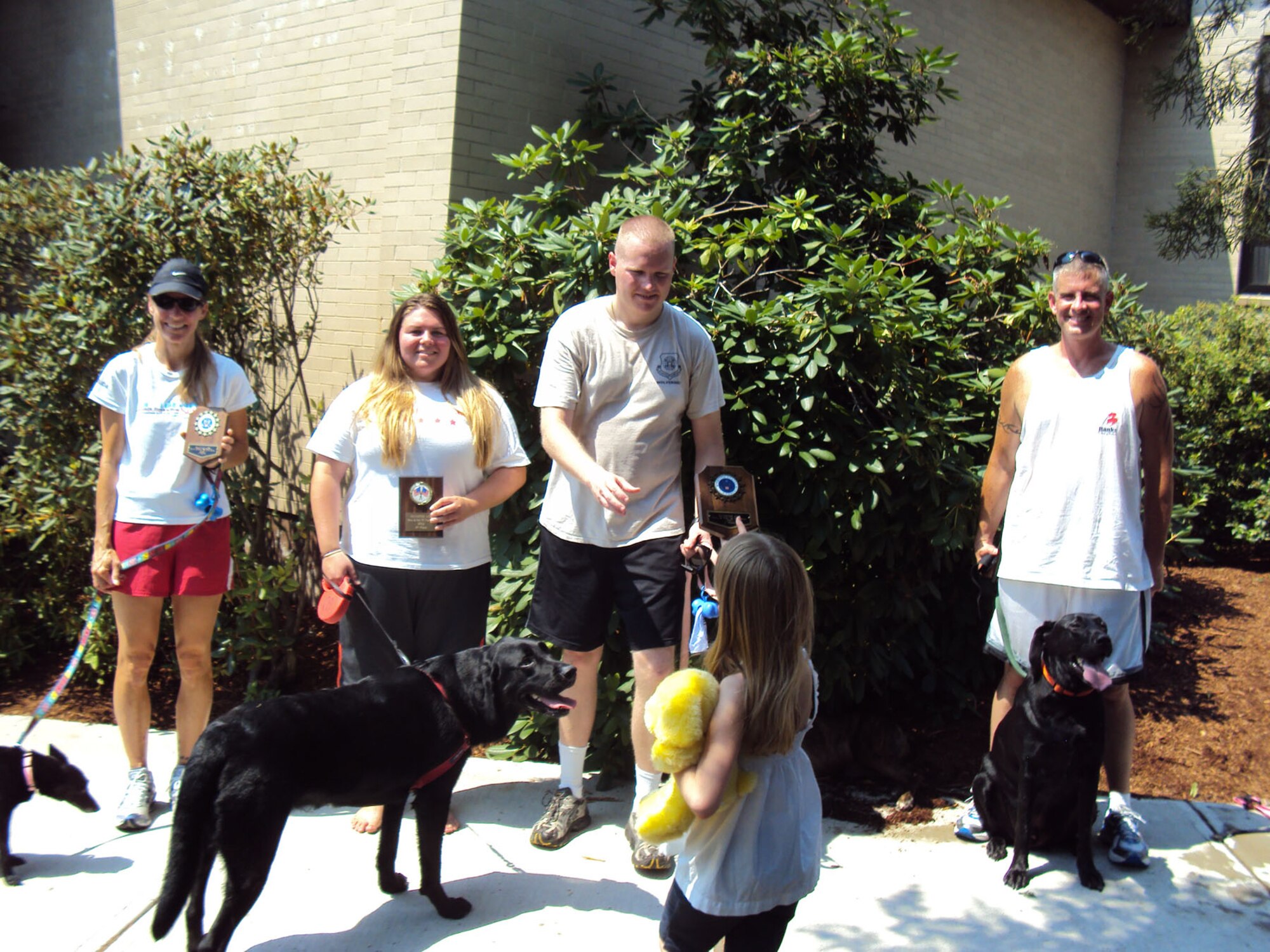 HANSCOM AIR FORCE BASE, Mass. – Emma Glashower hands the first place plaque to her father, Kyle, who ran with his dog, Dallas, in 20:03 during the Paws and Pals 5K at the Minuteman Commons Aug. 4. Jason Borchers (right) and his dog, Buddy, finished second in the male category, while Stephanie Fournier (left) and her dog, Sophi, were first and Jessica Gernert and her dog, Hershey, placed second amongst female runners. (Courtesy photo) 