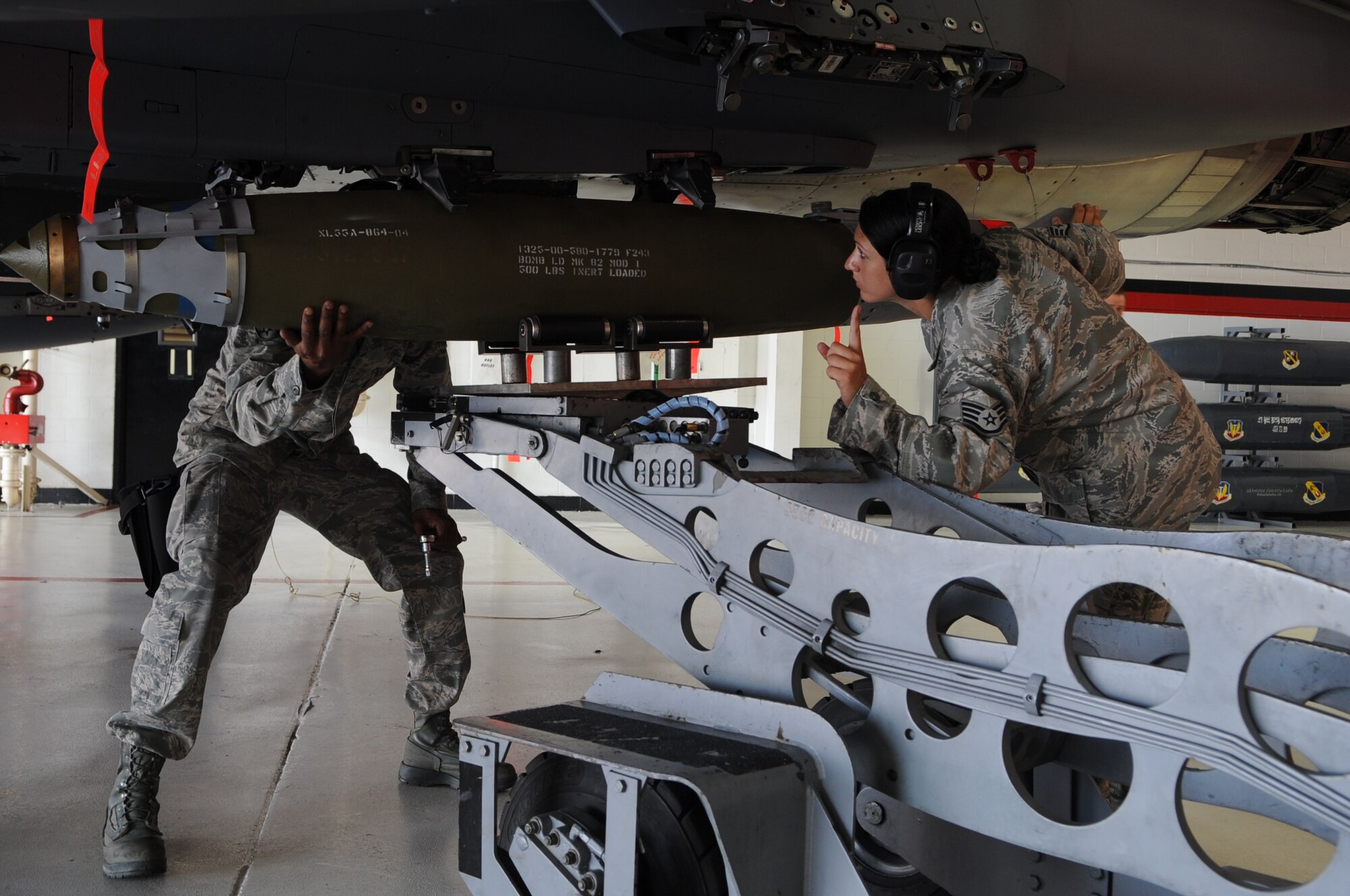 U.S. Air Force Staff Sgt. Valerie Scafidi, 333rd Aircraft Maintenance Unit weapons load crew chief, signals to raise a ground power unit-38 bomb as Airman Ulysses Richmond, 333rd AMU weapons load crew member, assists while loading an F-15E Strike Eagle for display on Seymour Johnson Air Force Base, N.C., Aug. 2, 2012. The aircraft was made up to simulate full battle ensemble in honor of Dyrk Burcie, a 4-year old living with terminal, stage four, pediatric liver cancer. (U.S. Air Force photo/Airman 1st Class Aubrey Robinson/Released)