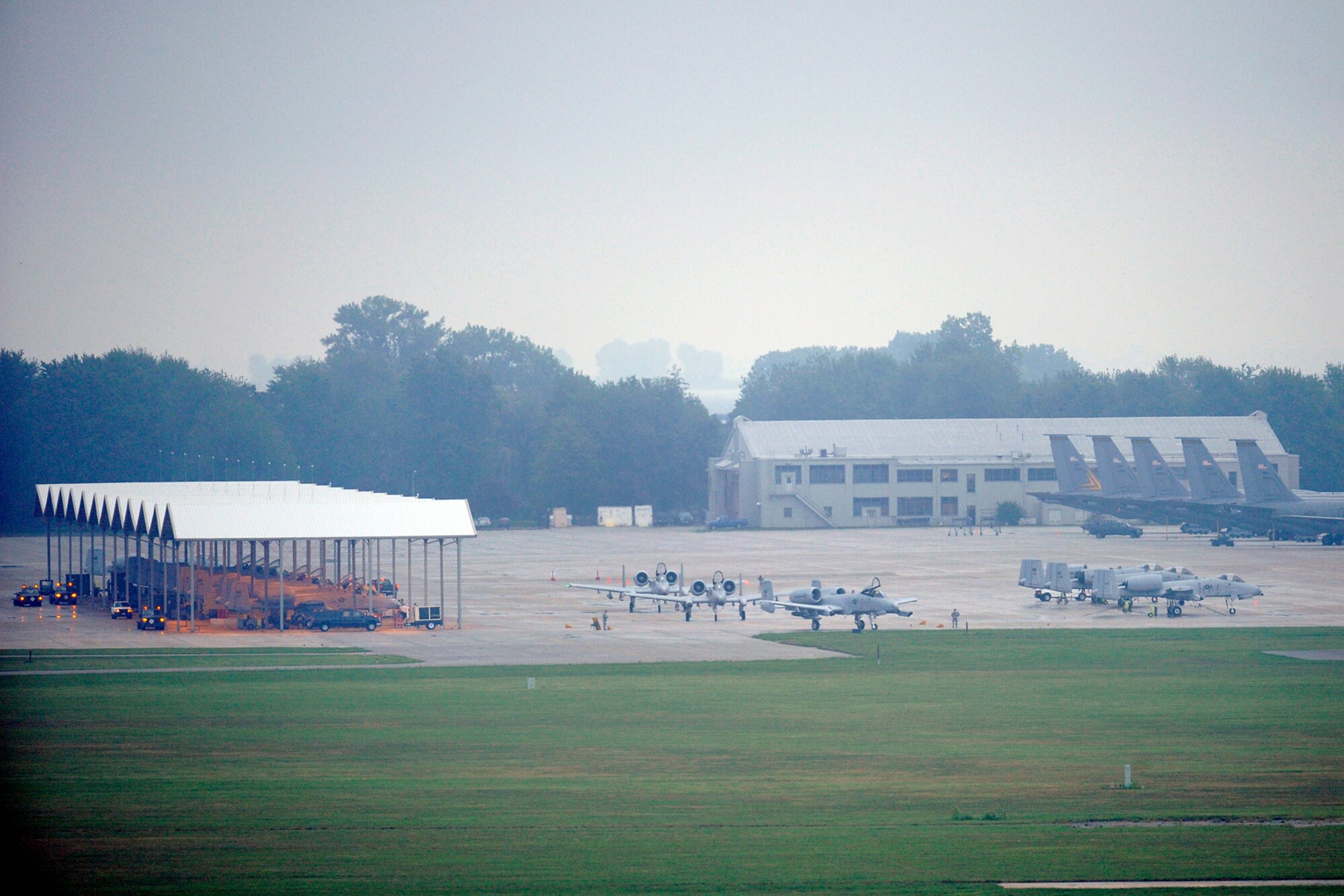 Seen from the air traffic control tower on the opposite side of the air field, three A-10 Thunderbolt II aircraft taxi out of the parking ramp area toward the active runway at Selfridge Air National Guard Base, Mich., Aug. 10, 2012. An orange glow can be seen under the structures at left, where Airmen were using work lights in an early morning rain to prepare for the day’s flying missions.  Airmen from the 107th Fighter Squadron, who fly the aircraft, and the 127th Maintenance Group, who maintain the aircraft, participated in a surge operation, launching and recovering a higher-than-usual number of aircraft, as part of a series of readiness training exercises taking place at the base in August. (Air National Guard photo by John S. Swanson)