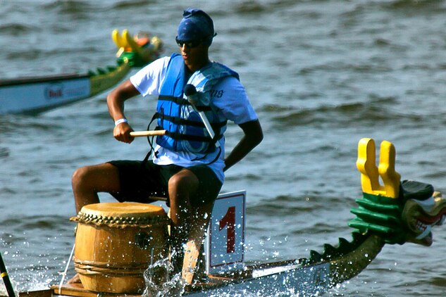 A Marine with Marine Wing Communication Squadron 28 from Cherry Point acts as a pace keeper for one of the teams participating in the dragon boat races on the Neuse River, Saturday, in Oriental, N.C. The pace keeper beats a drum so the rowers stay on the same beat to help guide the boat through the water faster.