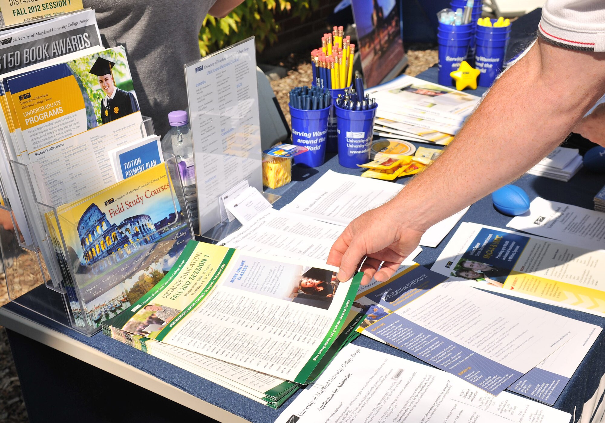 RAF MILDENHALL, England – Kevin Carrico, Airman and Family Readiness Center, picks up a course list from the University of Maryland University College information table during the college fair and barbecue Aug. 10, 2012, in Washington Square. Field representatives from colleges offering classes here and at RAF Lakenheath, representatives from the Airman and Family Readiness Center and a school liaison set up information tables for the event. (U.S. Air Force photo/Senior Airman Jerilyn Quintanilla) 