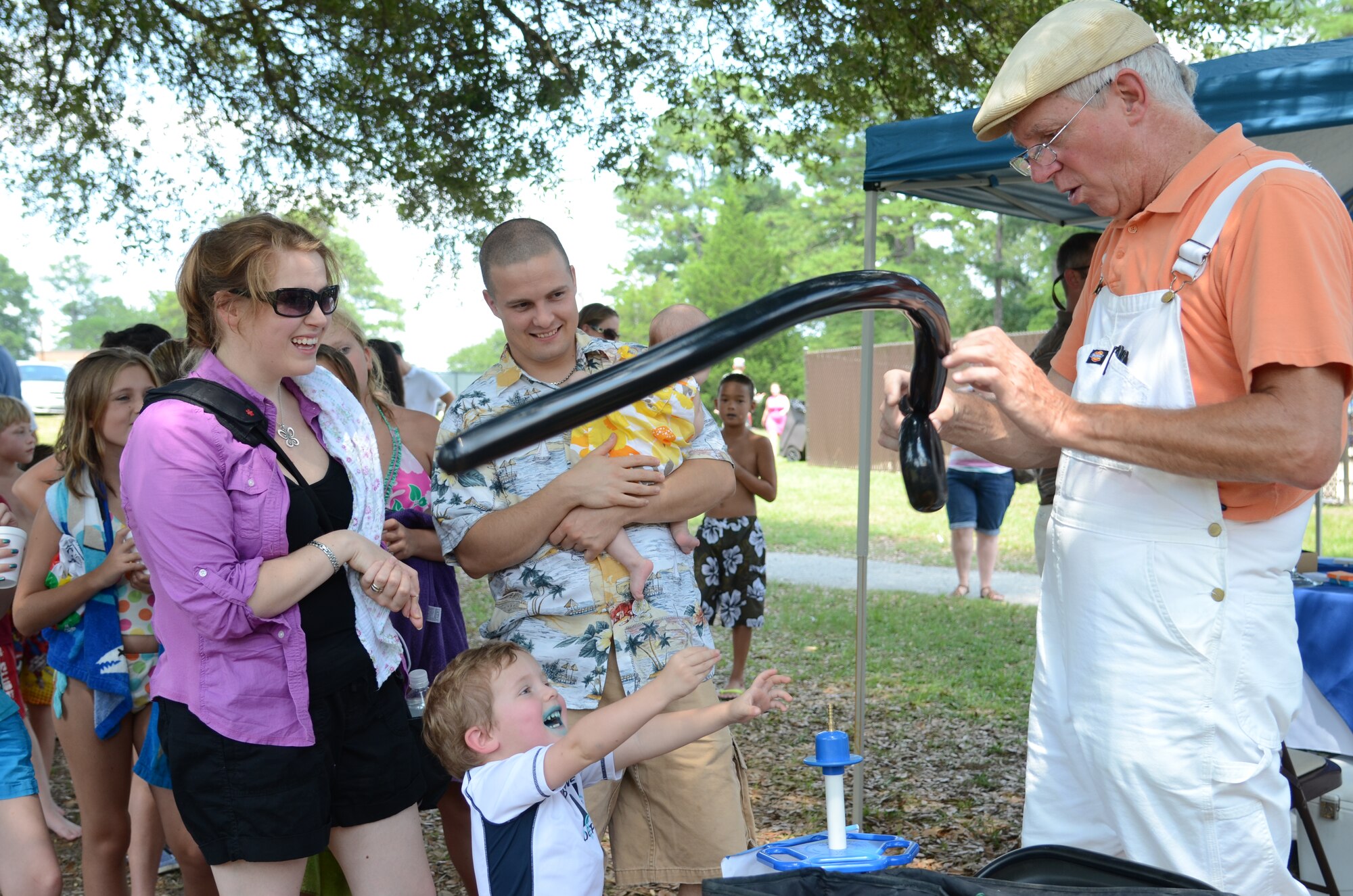 SHAW AIR FORCE BASE, S.C. - Marissa Witcher and her husband U.S. Air Force Airman 1st Class Greg Witcher, an intel analyst assigned to the 20th Operations Support Squadron watch as their son Charles reaches for a balloon from Randy “Balloon Dude” Bennett during the Summer Splash event outside Woodland Pool on Shaw Air Force Base, S.C., Aug. 13, 2012. More than 1,200 members of Team Shaw participated in the event that was sponsored by the city of Sumter, S.C., Farmer's Telephone Cooperative, Progress Energy and 20th Fighter Wing members.  Attendees were treated to free food, face painting, water games, music and snow cones. (U.S.  Air Force photo by Master Sgt. Cohen A. Young/Released)