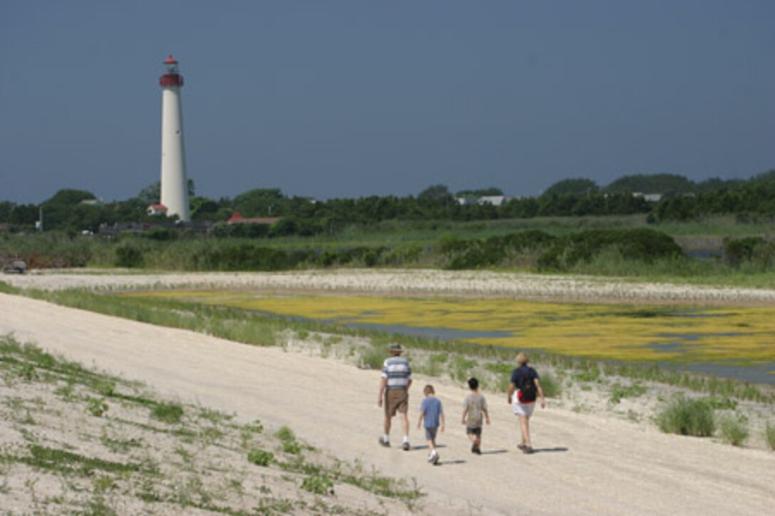 A family walks on a sandy path on the way to a lighthouse.