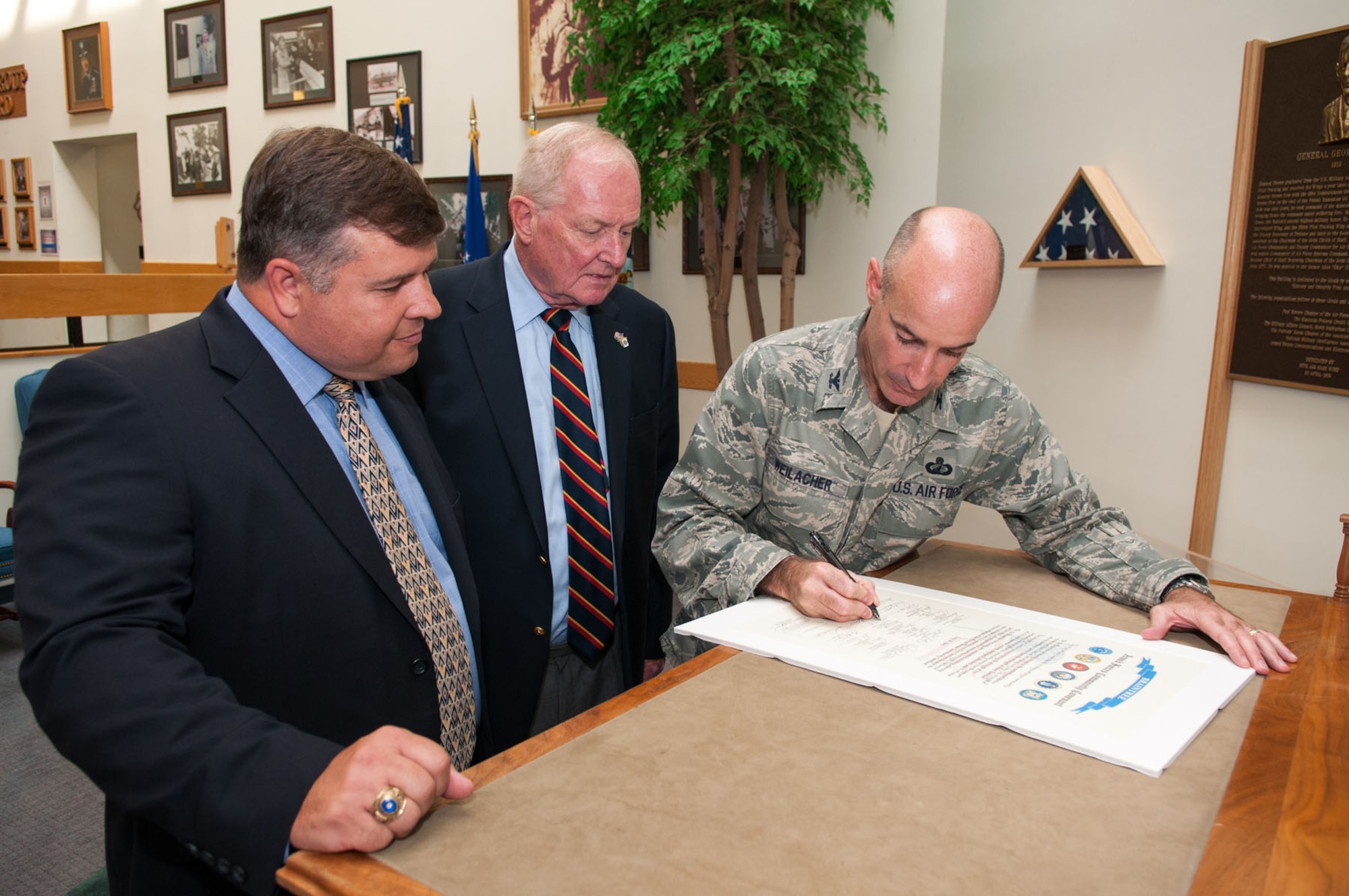 HANSCOM AIR FORCE BASE, Mass. – Retired Army Lt. Col. Fred Maguire (center), from the Association of U.S. Army, watches as Col. Lester A.  Weilacher, 66th Air Base Group commander, affixes his signature to the Community Covenant from the Town of Braintree, Mass., in the Brown Building atrium Aug. 10. Also taking part in the signing ceremony was Tom Fredericks, 66th Air Base Group deputy director. The covenant is designed to foster and sustain state and community partnerships to support military servicemembers, veterans and their families in the local community.  Braintree became one of 450 communities to sign a community covenant, a program which started in 2008. (U.S. Air Force photo by Rick Berry)