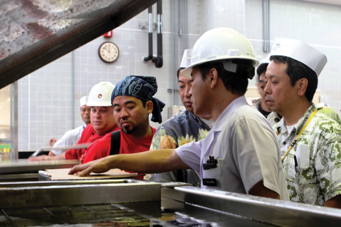 Takanori Takahara explains the functions of a cook tank to members of the Urasoe City Chamber of Commerce at the cook-chill facility at Camp Kinser Aug. 10. 