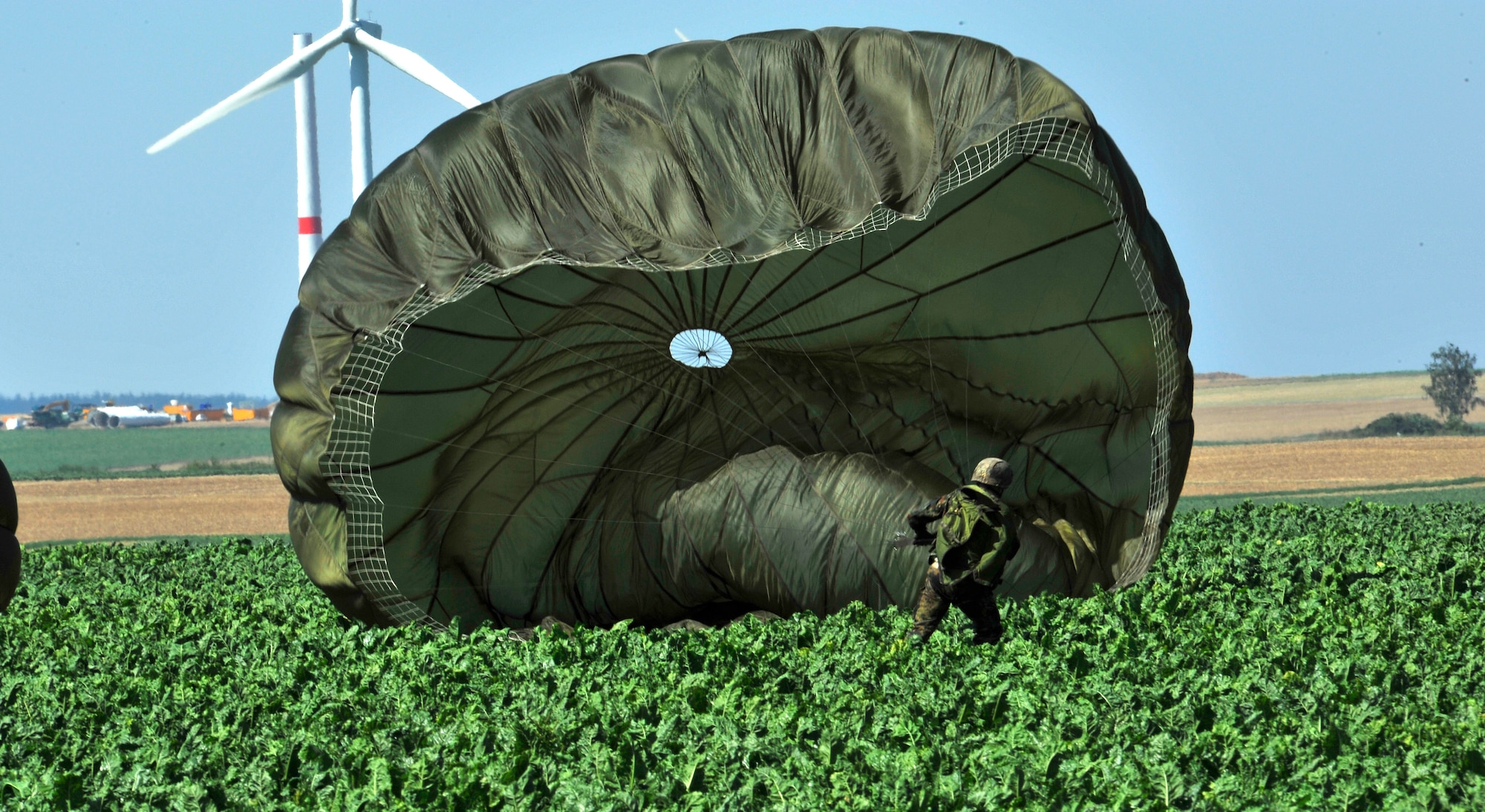 A German paratrooper attempts to pull in his chute in after landing in a field during International Jump Week 2012 near Alzey, Germany. Members of six NATO countries came together to trade jump tactics and techniques and got the opportunity to earn the other nation's jump wings. (U.S. Air Force photo/Airman 1st Class Trevor Rhynes)  