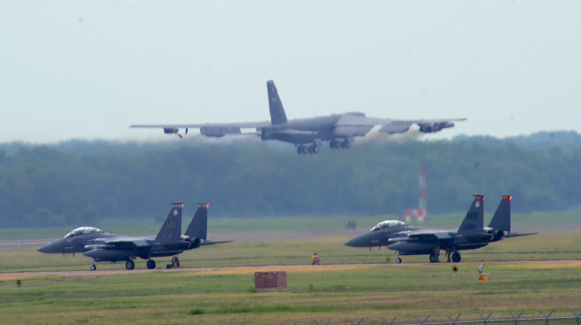 A B-52H Stratofortress flies over taxiing F-15E Strike Eagles on Barksdale Air Force Base, La., Aug. 15. The B-52 aircrews flew from Barksdale to Utah to participate in Exercise Combat Hammer, which evaluated the employment of precision guided munitions to ensure the weapons are fully functional and mission capable. (U.S. Air Force photo/Staff Sgt. Amber Ashcraft)(RELEASED)