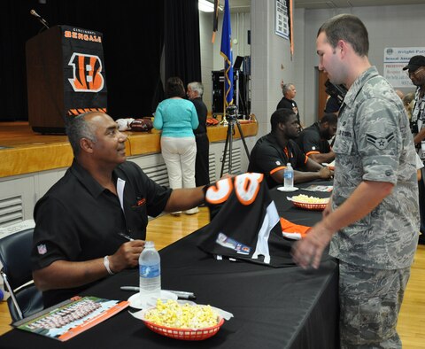 WRIGHT-PATTERSON AIR FORCE BASE, Ohio – Airman First Class Andrew Woods, 445th Operations Support Squadron, aircrew flight equipment journeyman, has Marvin Lewis, Cincinnati Bengals head coach, sign a Bengals football jersey at the Community and Airman Center here Aug. 6. Lewis and Bengals players Adam Jones, Jermaine Gresham and Geno Atkins plus Eric Ball, director of player relations, visited the base to meet with Airmen and their families and to talk about a special promotion for game tickets. (U.S. Air Force photo/Stacy Vaughn)