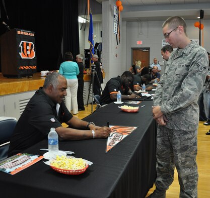 WRIGHT-PATTERSON AIR FORCE BASE, Ohio – Airman First Class Michael Petersen, 445th Operations Support Squadron, aircrew flight equipment journeyman, has Marvin Lewis, Cincinnati Bengals head coach, sign a Bengals pendant at the Community and Airman Center here Aug. 6. Lewis and Bengals players Adam Jones, Jermaine Gresham and Geno Atkins plus Eric Ball, director of player relations, visited the base to meet with Airmen and their families and to talk about a special promotion for game tickets. (U.S. Air Force photo/Stacy Vaughn)