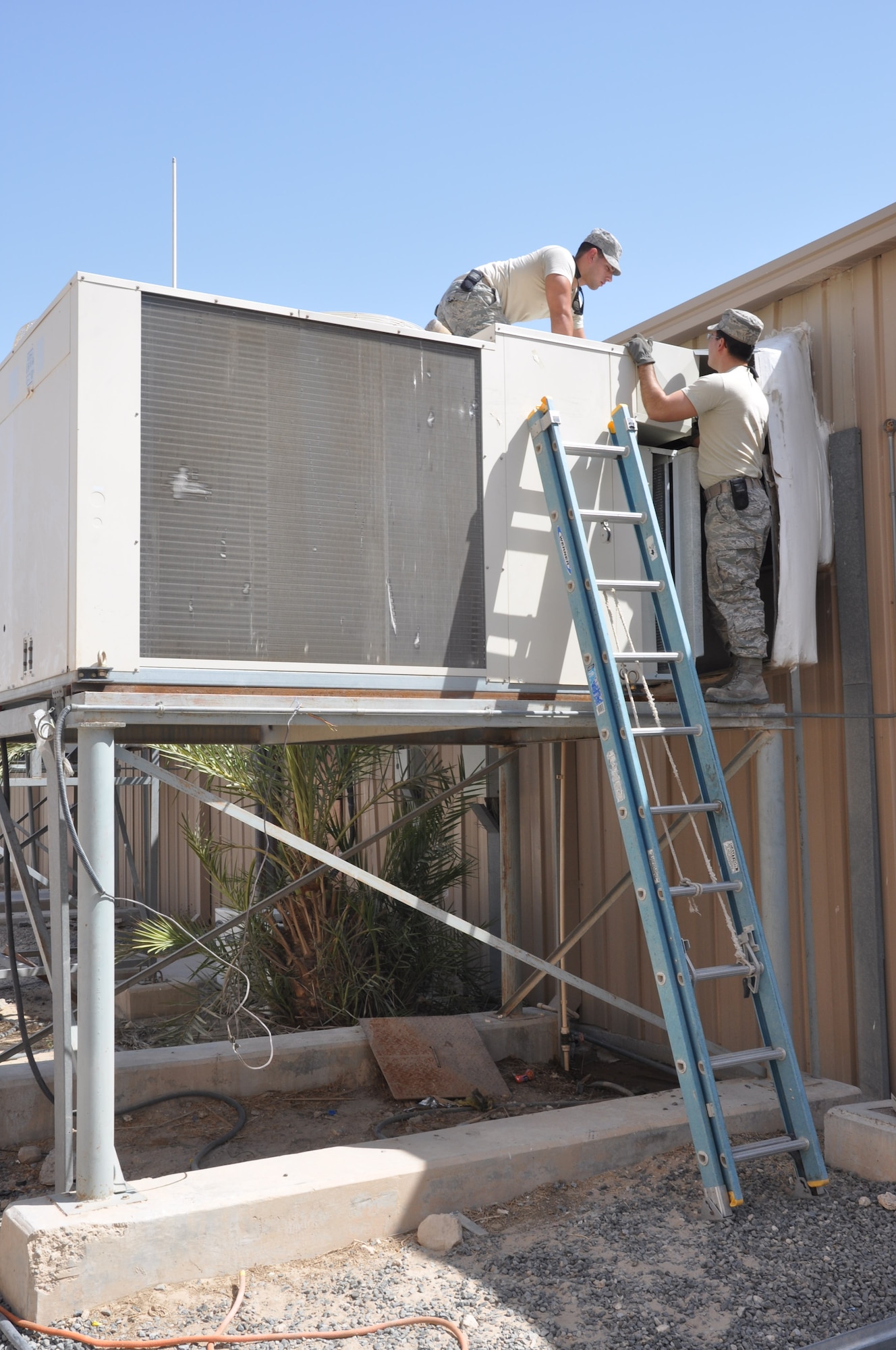 SOUTHWEST ASIA - Senior Airman Javier Rodriguez (top) and Senior Airman Carlos Colón, Heating, Ventilation and Air Conditioning Craftsmen, work to repair a segment of metal sheeting on an HVAC unit at the 386th Air Expeditionary Wing. Both Airmen are deployed members of the Puerto Rico Air National Guard.