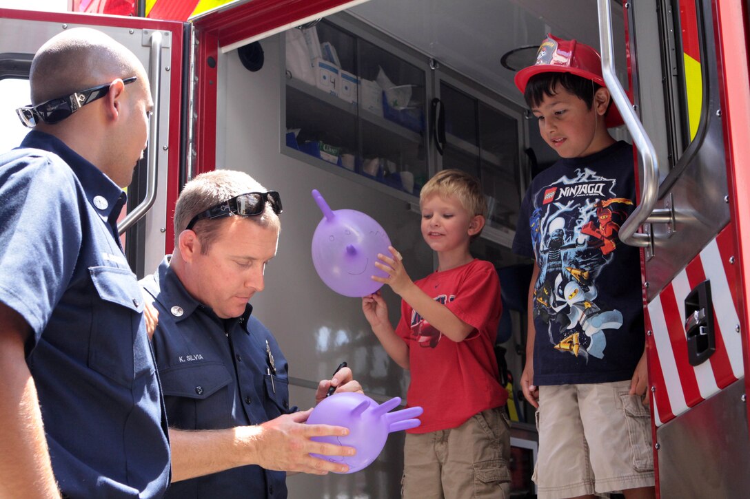 Firefighters with Camp Pendleton Fire Department draw symbols on Kaden Rivera's, 6, right, glove balloon during the luncheon in his honor at Fire Station 8 on Camp Pendleton, Aug. 18. Rivera also explored the inside of the ambulance that transported him to the hospital.