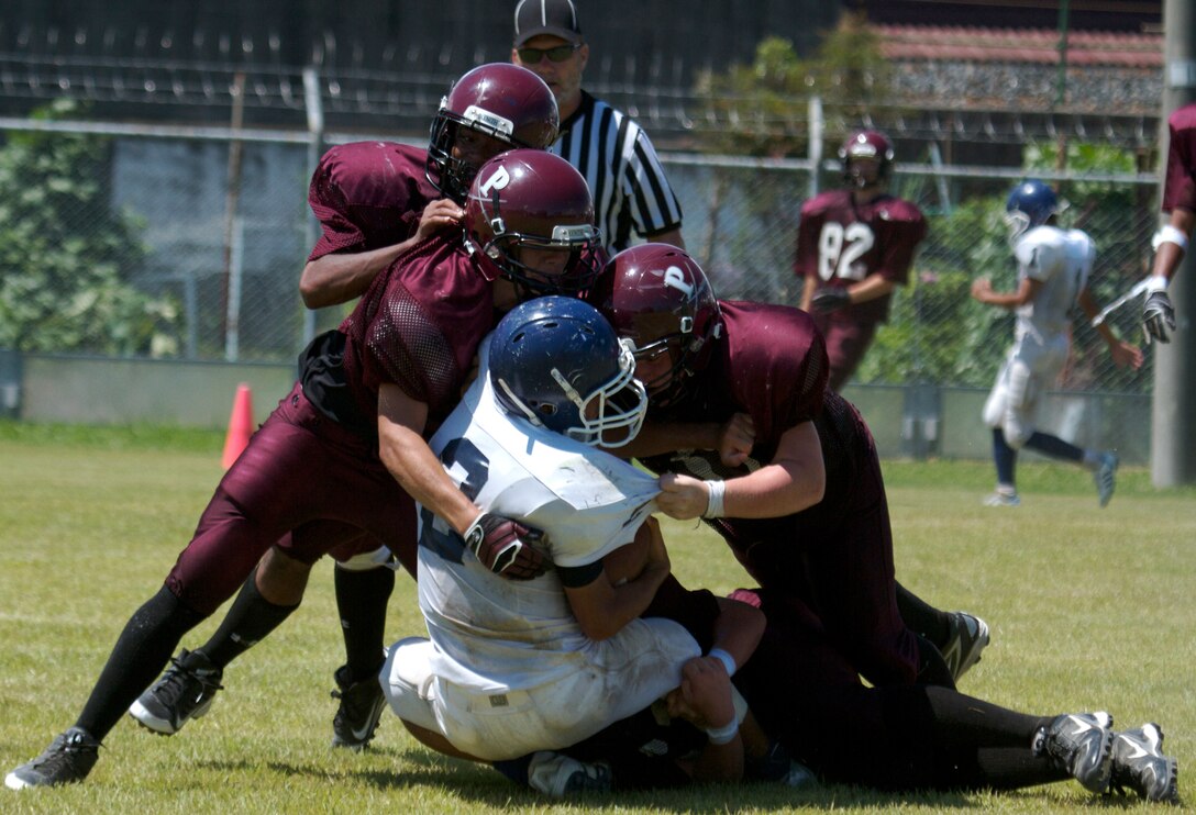 Several Matthew C. Perry High School Samurai football players swarm a Sotoku High School Fighting Ducks football player during a scrimmage game at the M.C. Perry football field here Aug. 19, 2012. The scrimmage capped off a two-day football camp between the schools where the players learned a variety of football techniques. This is the first time in eight years M. C. Perry has fielded a full-contact football team.