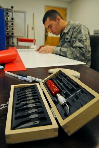A craft knife and razors sit in a box while Airman 1st Class Dylan Fox, 2nd Maintenance Squadron, removes excess vinyl from a vinyl sheet on Barksdale Air Force Base, La., Aug. 20. The vinyl is used to create graphics and tail markings for aircraft and equipment. 2 MXS Airmen use an assortment of blades to aid them in removing the vinyl. The knives are razor sharp so Airmen must use extreme caution so they do not injure themselves or damage the design. (U.S. Air Force photo/Airman 1st Class Micaiah Anthony)(RELEASED)