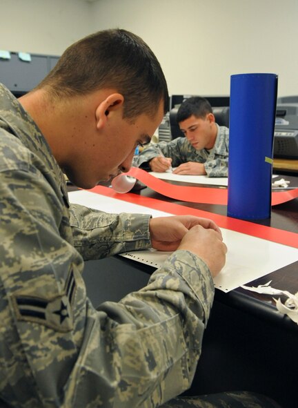 Airman 1st Class Dylan Fox and Senior Airman Robert Schwab, 2nd Maintenance Squadron, remove excess vinyl from a vinyl sheet on Barksdale Air Force Base, La., Aug. 20. The vinyl is used to create graphics and tail markings for aircraft and equipment. 2 MXS Airmen use extreme caution when removing the excess vinyl so they do not damage the design or injure themselves. (U.S. Air Force photo/Airman 1st Class Micaiah Anthony)(RELEASED)