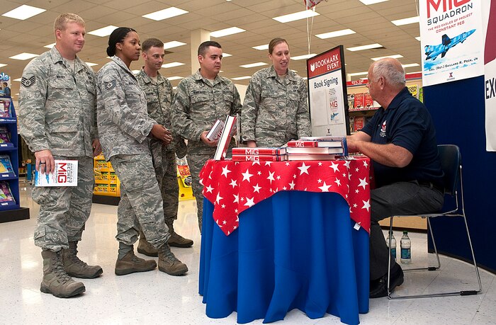 Retired Col. Gaillard Peck , signs autographs in his book,"America's Secret MIG Squadron", for Airmen during a book signing at the Nellis Base Exchange Aug. 17, 2012, at Nellis Air Force Base, Nev. The book tells the story of how a group of military pioneers used their experiences and knowledge to form a training paradigm for fighter pilots. (U.S. Air Force photo by Staff Sgt. Christopher Hubenthal)