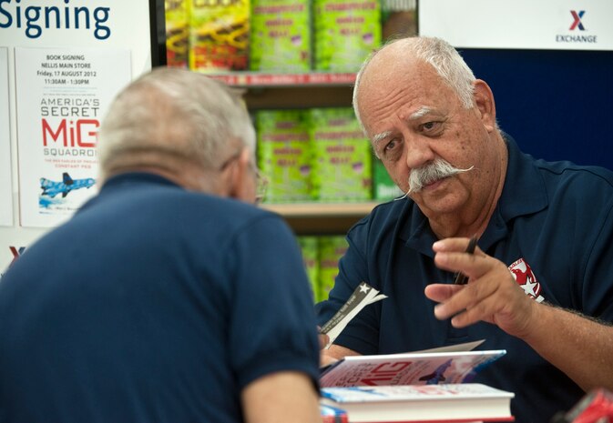 Retired Col. Gaillard Peck, autographs his book,"America's Secret MIG Squadron", during a book signing at the Nellis Base Exchange Aug. 17, 2012, at Nellis Air Force Base, Nev. The book tells the story of how a group of military pioneers used their experiences and knowledge to form a training paradigm for fighter pilots. (U.S. Air Force photo by Staff Sgt. Christopher Hubenthal)