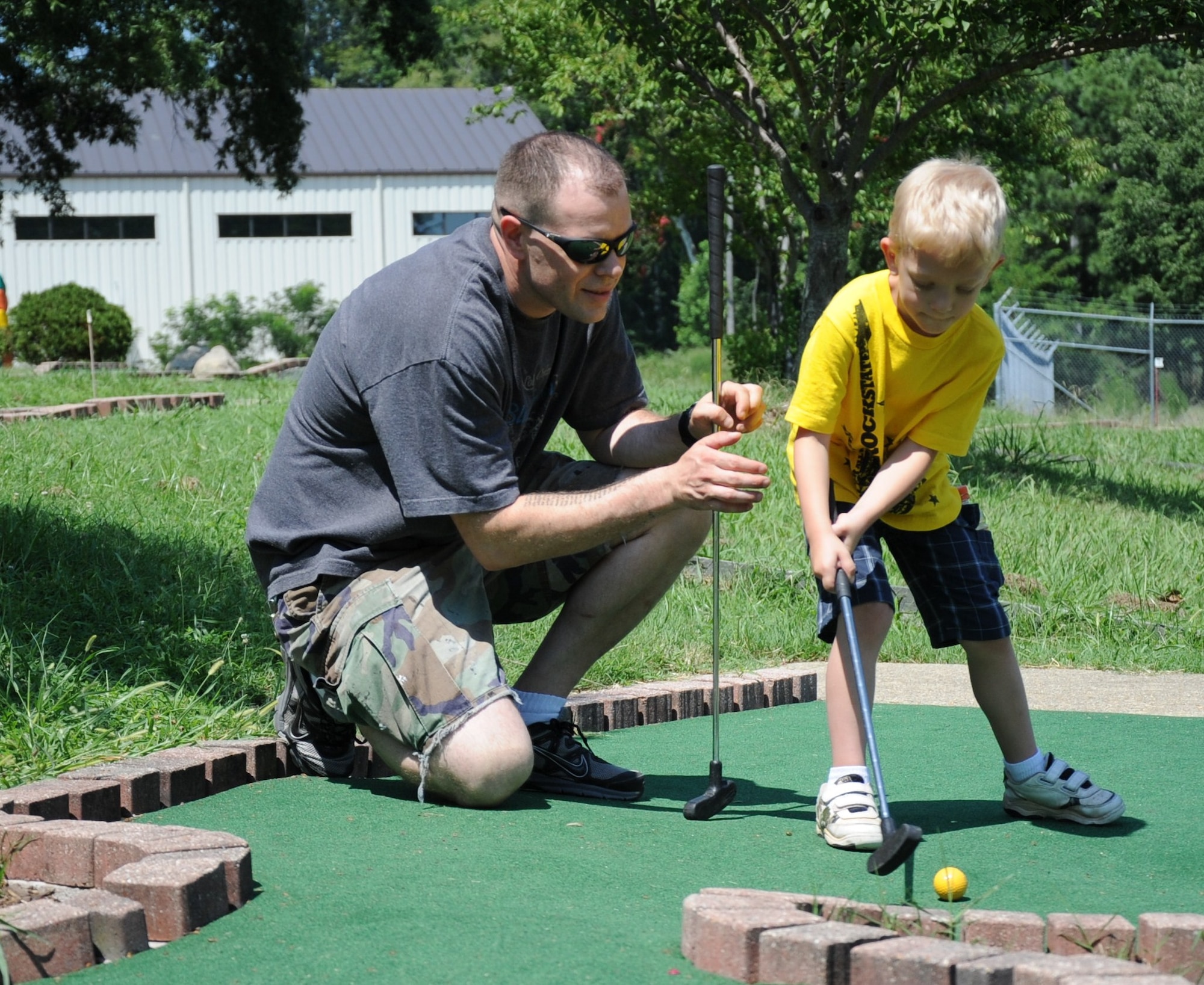 U.S. Army Spc. Isaac Stevens, a Soldier assigned to the 53rd Transportation Battalion, helps his son William line up a putt on the mini-golf course at Fort Eustis' mini-park Aug. 17, 2012. The mini-park's attractions are competitively priced, and allow military families an opportunity to enjoy the activities for a fraction of the price compared to off-base facilities. (U.S. Air Force photo by Senior Airman Jason J. Brown/Released)