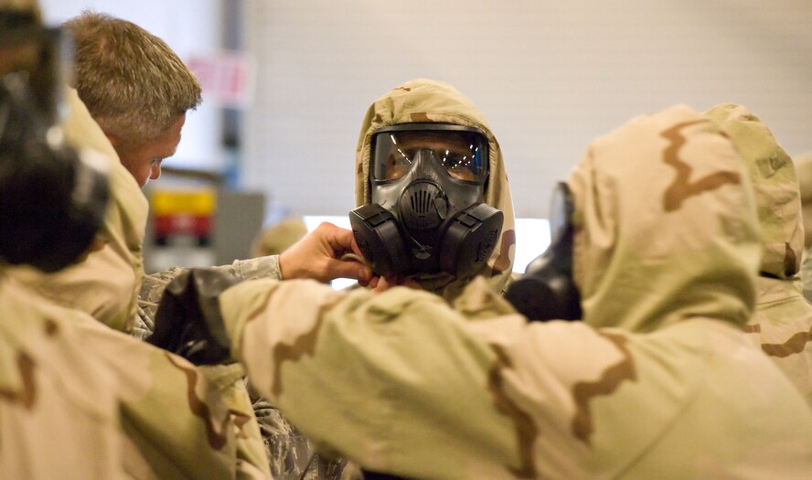 Tech. Sgt. Gregory Foster, left background, a member of the 436th  Civil Engineer Squadron Emergency Management Section, ensures a student’s chemical-protective suit is properly fastened during a Chemical Biological Radiological and Nuclear survival skills training class Aug. 9, 2012, at Dover Air Force Base, Del. Students also demonstrated buddy system checks, helping each other don their gear. (U.S. Air Force photo by Roland Balik)