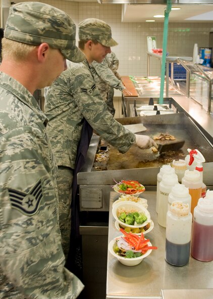 U.S. Air Force Staff Sgt. Dustin McBroom, 7th Force Support Squadron (left), mixes sauces with vegetables while Airman 1st Class Steven Roberts, 7th FSS, cooks meats on the grill for an Asian style stir-fry as a special meal Aug. 16, 2012, at the Longhorn Dining Facility on Dyess Air Force Base, Texas. The dining facility features meals from several cultures each month to offer variety to its customers. Dyess begins the second phase of food operations as part of the Food Transformation Initiative beginning Oct. 1. The FTI program is designed to improve the quality, variety, and availability of food service operations. FTI will adjust installation food service operations to meet the lifestyles, needs and preferences of customers, and will restore a sense of community by expanding the eligibility of customers who can use the facilities. (U.S. Air Force photo by Airman 1st Class Peter Thompson/ Released)