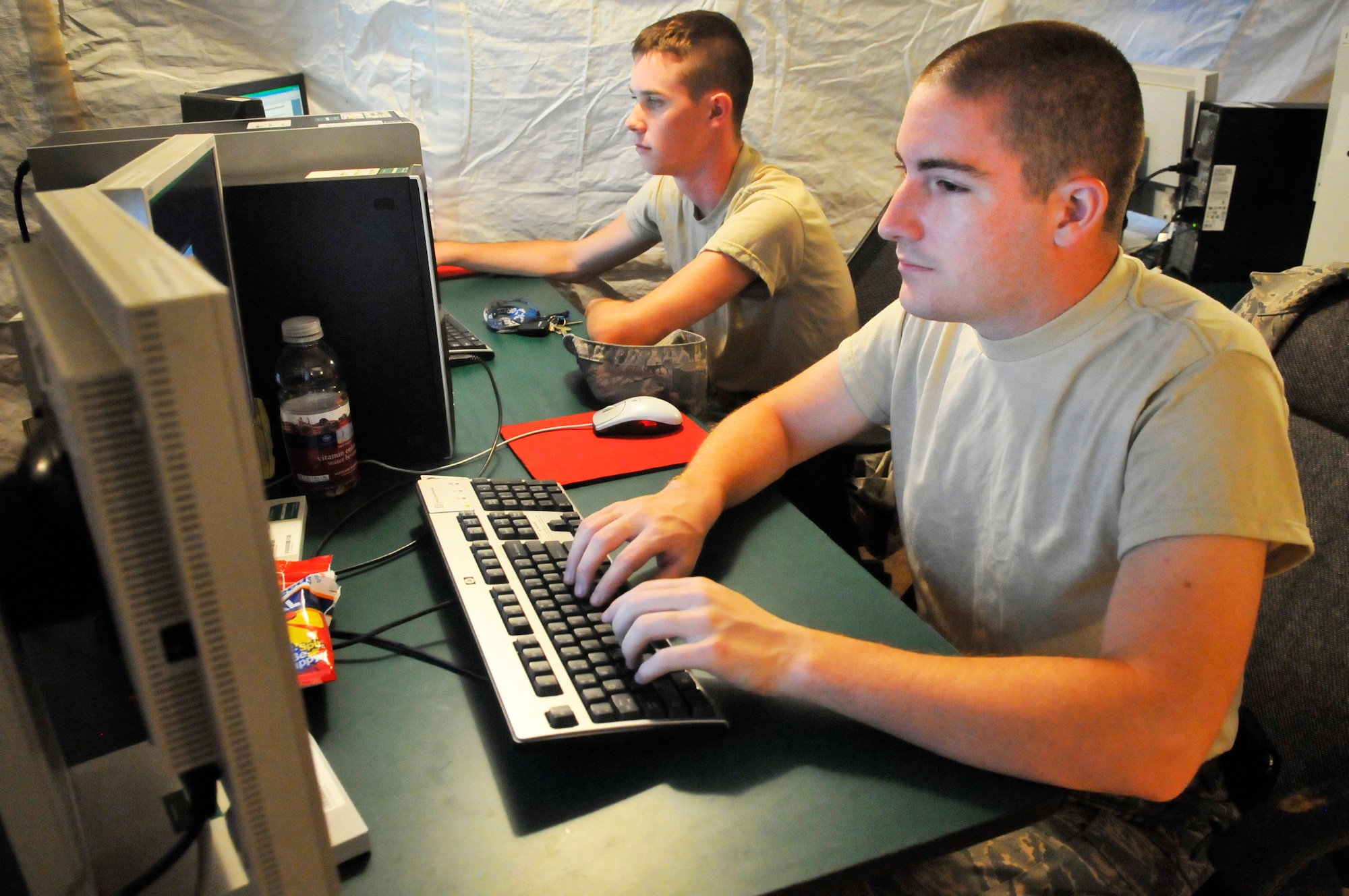 Airmen 1st Class Nicholas Brown, front, and Phil Terry, work in a tent behind Bldg. 963. The 51st Combat Communications Squadron have set up temporary work centers in and around Bldg. 963 including three tents with A/C, generators, etc. while air conditioning work is being done in that building. (U. S. Air Force photo/Sue Sapp)