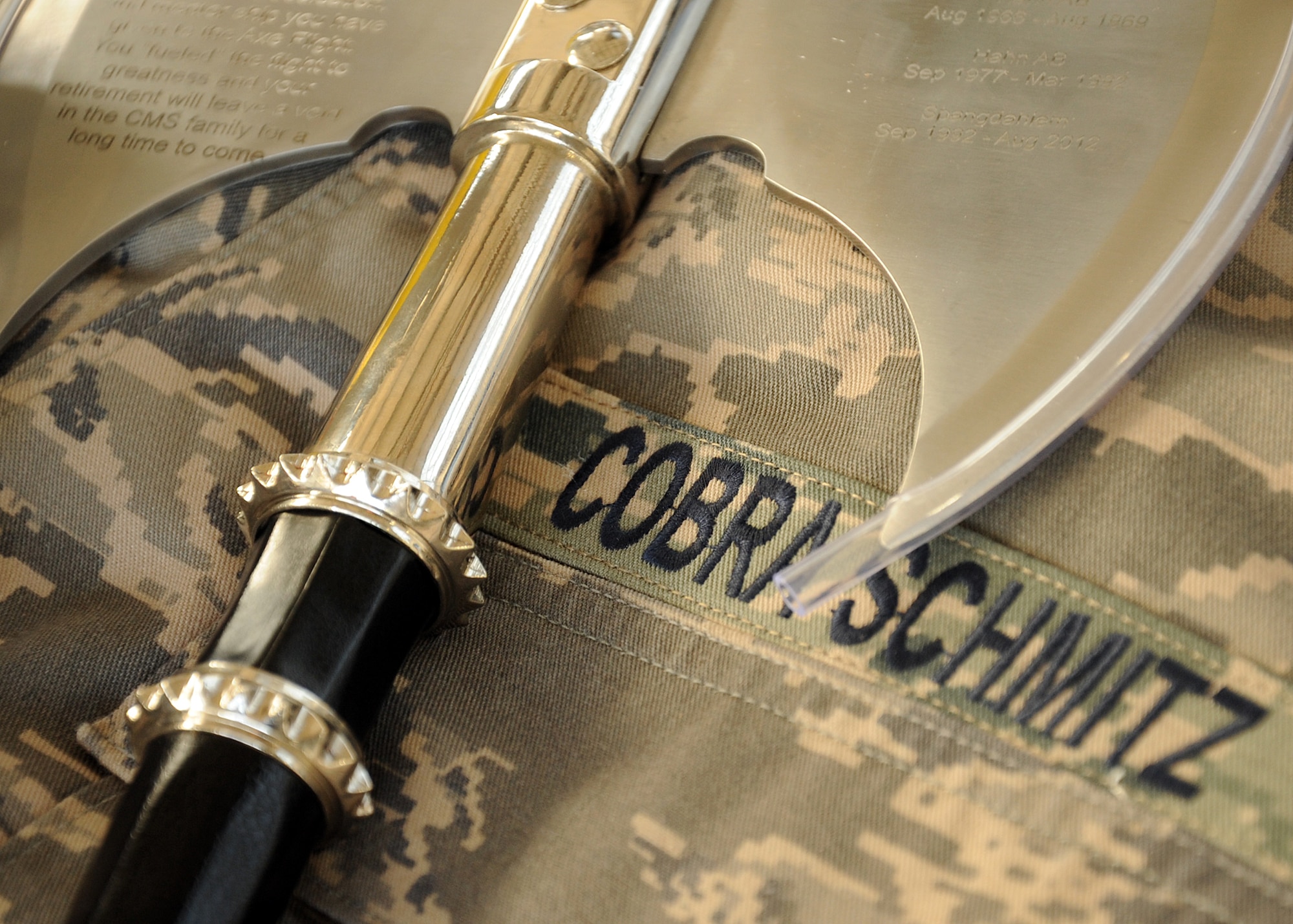 SPANGDAHLEM AIR BASE, Germany – An axe rests upon a custom Airman Battle Uniform blouse during the retirement ceremony of Alois Schmitz, 52nd Component Maintenance Squadron fuels systems repair shop, Aug. 17 in Hangar 3 here. The 52nd CMS Accessories Flight presented the axe to Schmitz as a parting gift. The blouse name tape reads “Cobra Schmitz,” which was Schmitz unofficial radio call sign. (U.S. Air Force photo by Staff Sgt. Daryl Knee/Released)