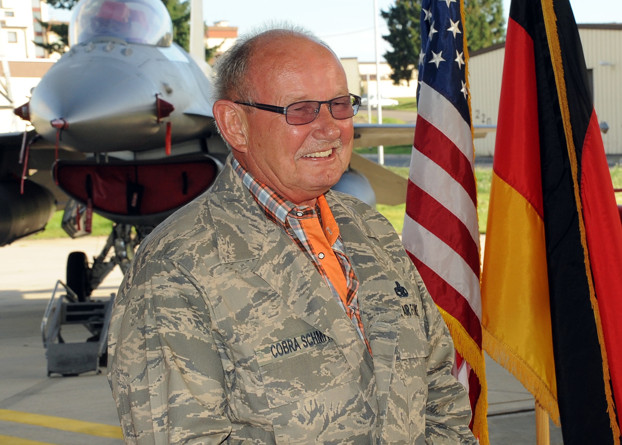 SPANGDAHLEM AIR BASE, Germany – Alois Schmitz, 52nd Component Maintenance Squadron fuels systems repair shop, listens during his retirement ceremony Aug. 17 here to coworkers speak about his near four-decade career. Schmitz, after having donned a custom Airman Battle Uniform blouse, took the podium and thanked the more than 100 Airmen, family and friends who had attended the ceremony. The name tag on the uniform reads “Cobra Schmitz,” which was Schmitz’ unofficial radio call sign. (U.S. Air Force photo by Staff Sgt. Daryl Knee/Released)