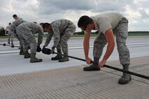 Airmen from the 4th Civil Engineer Squadron power production shop install rubber spacing donuts to a pendant cable for a cable engagement exercise on Seymour Johnson Air Force Base, N.C., Aug. 21, 2012. The Airmen evenly space out rubber donuts to keep the cable several inches off the runway, allowing the F-15E Strike Eagle to successfully employ its barrier hook. (U.S. Air Force photo/Airman 1st Class John Nieves Camacho/Released)