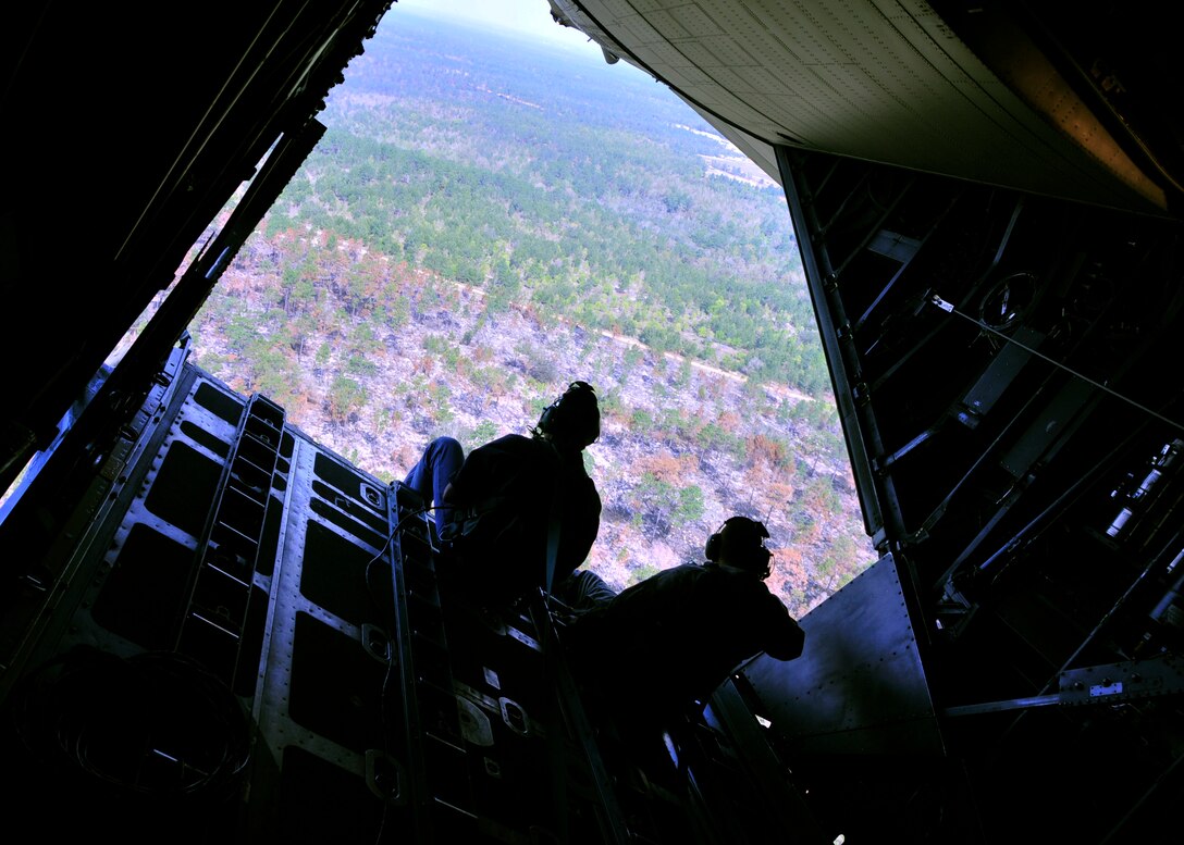 A U.S. Department of Agriculture wildlife biologist, left, and a military videographer are silhouetted aboard the open ramp of a 919th Special Operations Wing MC-130 as it banks over woodlands near Duke Field, Fla. The Air Force Reserve wing supported the department’s request for an aerial photography flight to document wildlife habitats that can create aviation hazards, such as bird strikes, at Duke Field and Eglin Air Force Base. (U.S. Air Force photo/Dan Neely)