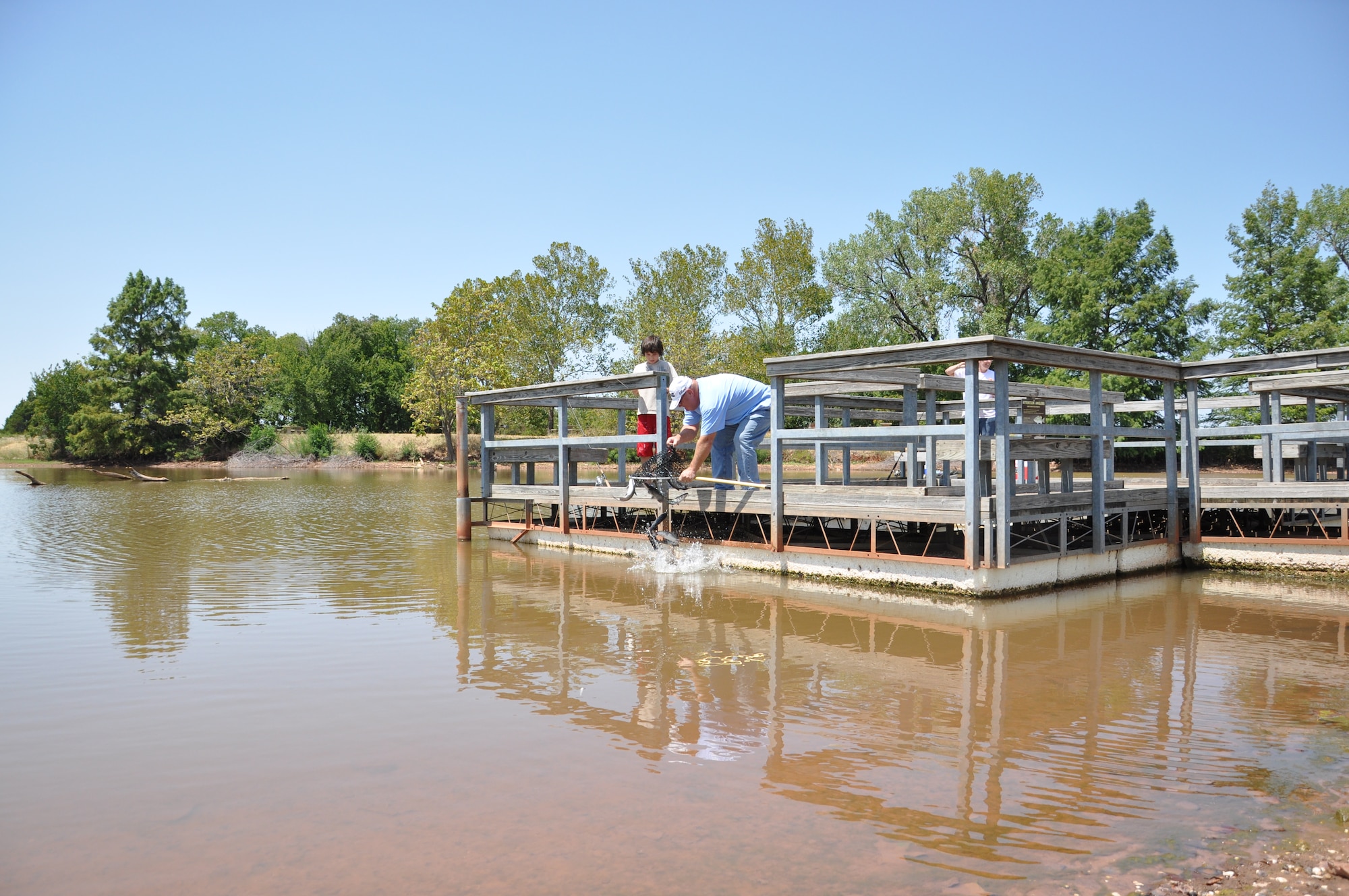 Environmental specialist Tim Taylor releases channel catfish as a young fisherman prepares for what he hopes to be a bountiful catch. (Air Force photo by Brion Ockenfels)