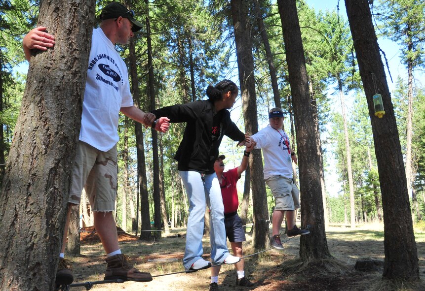 Master Sgt. Daniel Merrilll, holds on to a tree while Senior Airman Odessa Flores reaches her hand out to Bill Baker to proceed to the next step in the tight rope team challenge Aug. 22, 2012 at Adventure Dynamics in Nine Mile Falls, Washington. Merrill, Flores and Baker are all members of the 92nd Security Forces Squadron. (U.S. Air Force photo by Airman 1st Class Earlandez Young) 