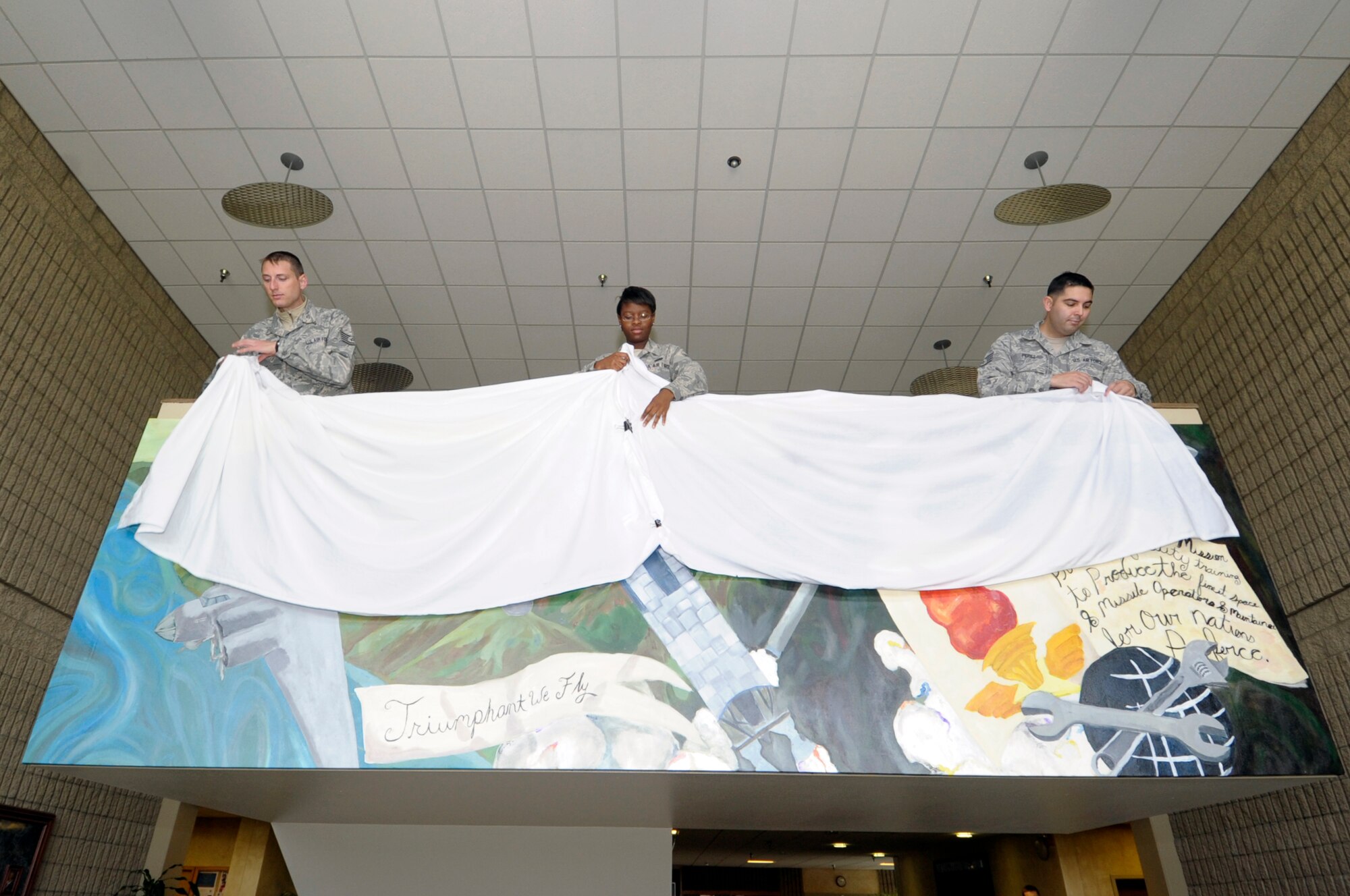 VANDENBERG AIR FORCE BASE, Calif. -- 381st Training Support Squadron members, Tech. Sgt. Trevor McIntyre, Airman 1st Class Eboni Alexander and Staff Sgt. Rafael Perez, unveil a mural representing the heritage of the 381st Training Group during a ceremony here, August 23, 2012. Alexander designed the mural and led the team depicting the 3 main eras of the unit; the 381st Bombardment Group, the 381st Strategic Missile Wing, and the 381st Training Group. (U.S. Air Force photo/Jerry E. Clemens Jr.)