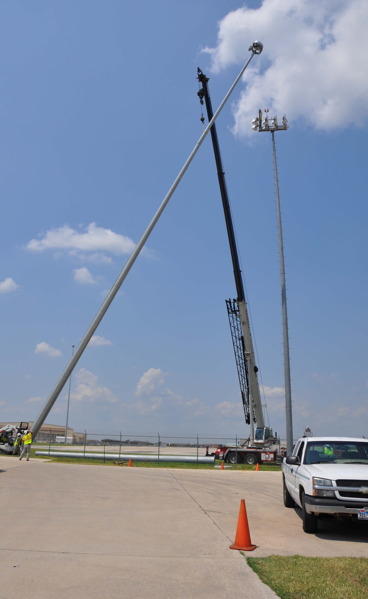 Contract crewmembers observe the progress as a crane lifts a light pole from the ground into position. The pole is one of 10 being erected on the flightline of the 433rd Airlift Wing flightline at Joint Base San Antonio-Lackland, Texas. (U.S. Air Force photo/ Senior Airman Viola M Hernandez)