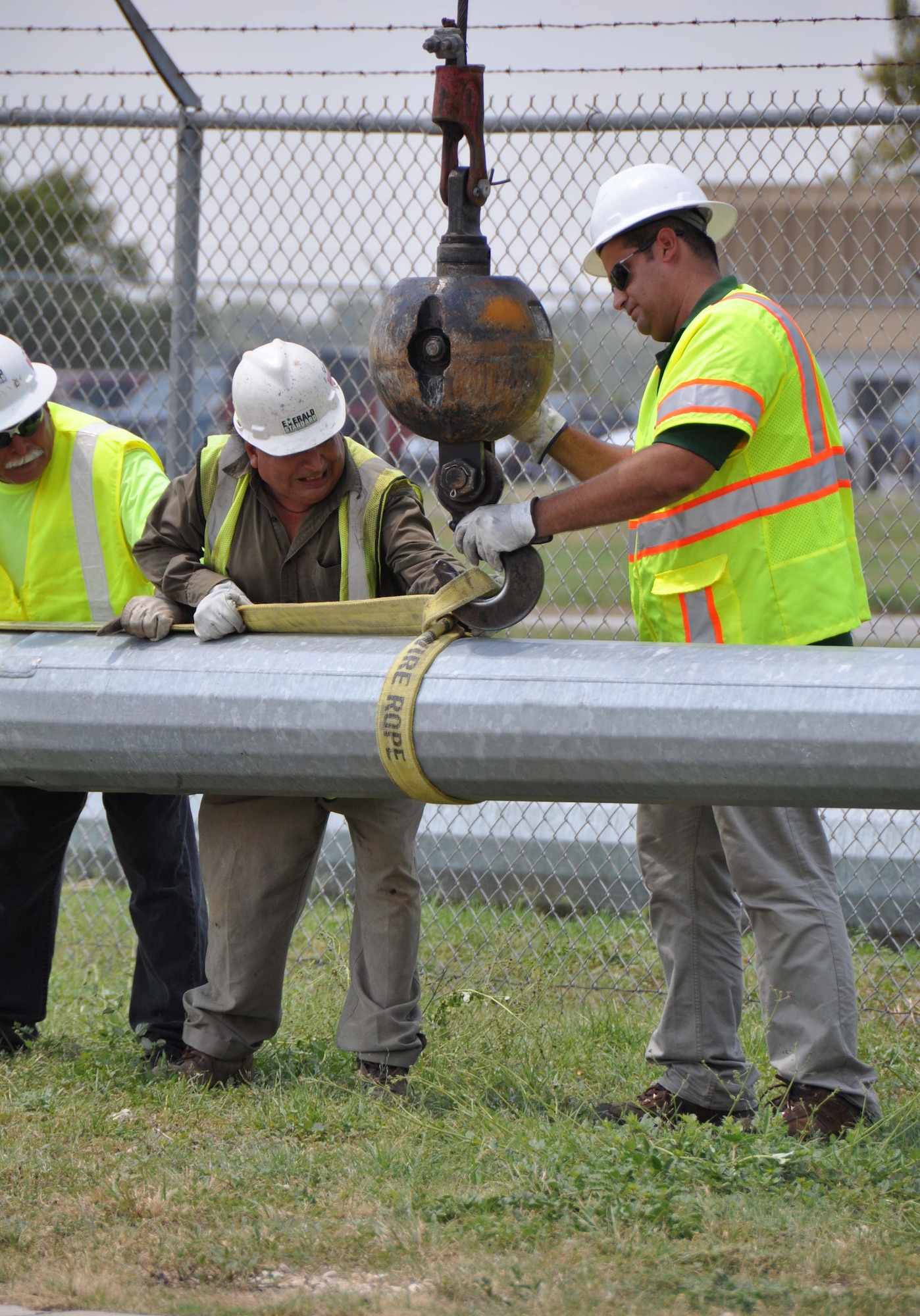 Emerald Standard Services Inc. crewmember secures the crane hook to a piece of thick wire rope while his coworkers hold the rope taut. The wire rope will be used to erect one of the new light poles which have been erected on the flightline of the 433rd Airlift Wing at Joint Base San Antonio-Lackland, Texas. (U.S. Air Force photo/Senior Airman Viola M. Hernandez) 
