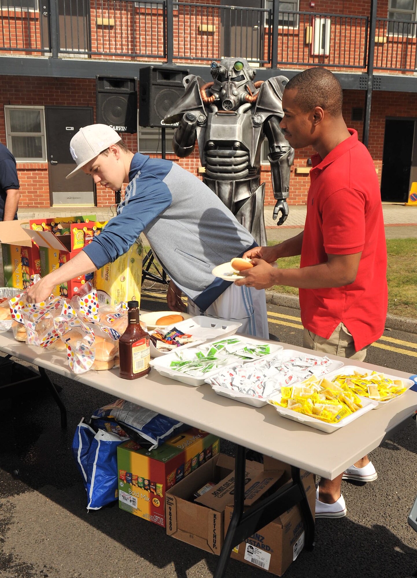 RAF MILDENHALL, England – From left, Senior Airman Andrew Flint, 100th Communications Squadron, and Airman 1st Class Jerry Jackson III, 100th Air Refueling Wing command post, go through the food line at the Unaccompanied Airmen Appreciation Day Aug. 23, 2012, in the Bob Hope Community Center parking lot. Members of the Chiefs’ Group grilled approximately 600 hamburgers and hotdogs for the event. The food was donated by several clubs and organizations sponsoring the event. (U.S. Air Force photo/Senior Airman Jerilyn Quintanilla)