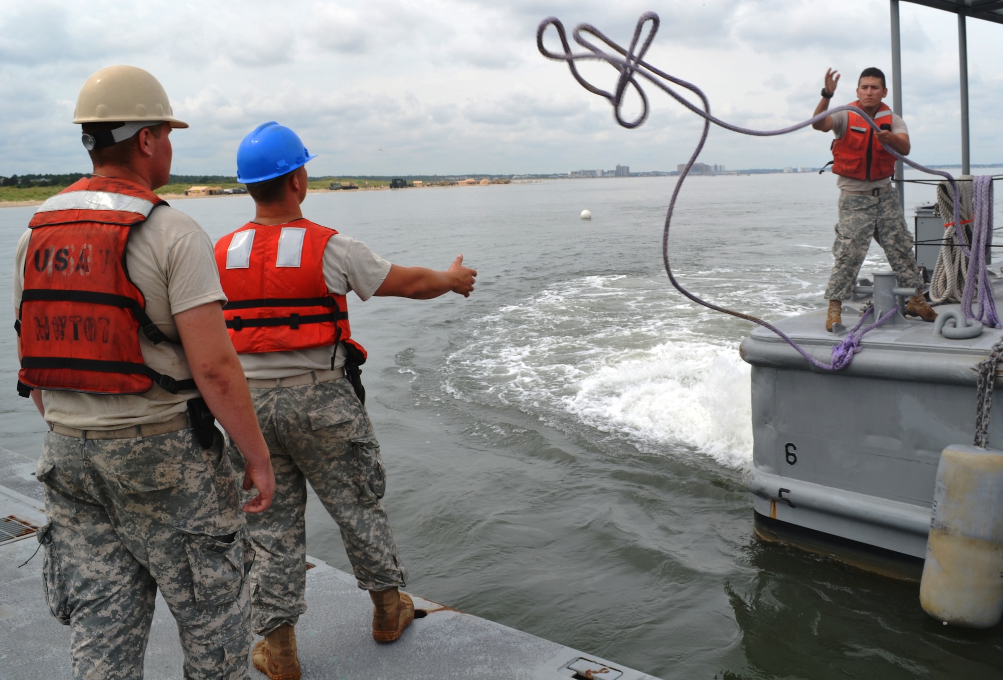 U.S. Army Pfc. Juan Guebara, right, a watercraft engineer assigned to the 7th Sustainment Brigade, tosses a line to two Soldiers on the main causeway during a Joint Logistics Over the Shore exercise at Fort Story, Va., Aug. 21. This exercise involves both U.S. Army and Navy personnel interacting to accomplish the mission. (U.S. Army photo by Staff Sgt. Alexander Burnett/ Released)