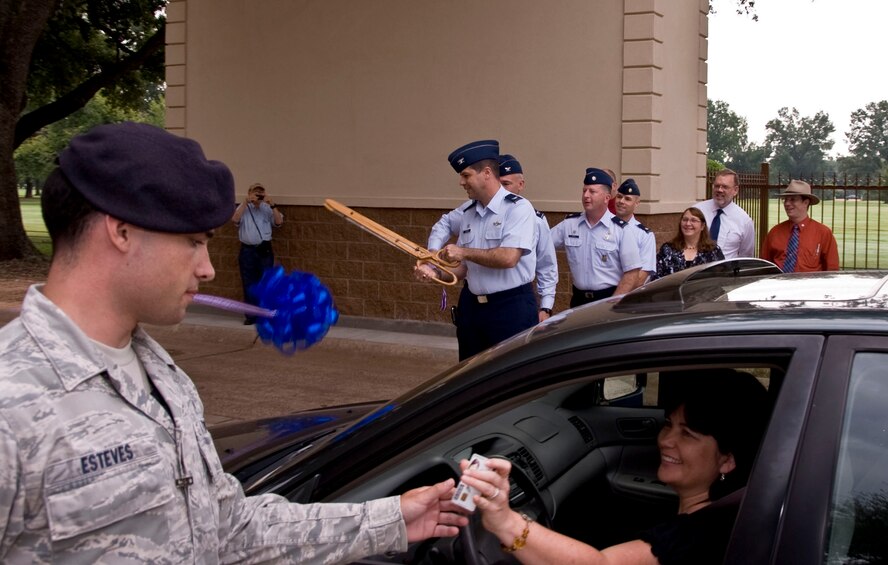 Col. Andrew Gebara, 2nd Bomb Wing commander, cuts the ribbon during the re-opening of the West Gate as Airman 1st Class Mauricio Esteves, 2nd Security Forces Squadron, checks the identification card of Barbara Makamson, 2nd Contracting Squadron, on Barksdale Air Force Base, La., Aug. 27. The $415,000 project now provides 2 SFS members cover from weather and enhances base security. (U.S. Air Force photo/Senior Airman La?Shanette V. Garrett)(RELEASED) 