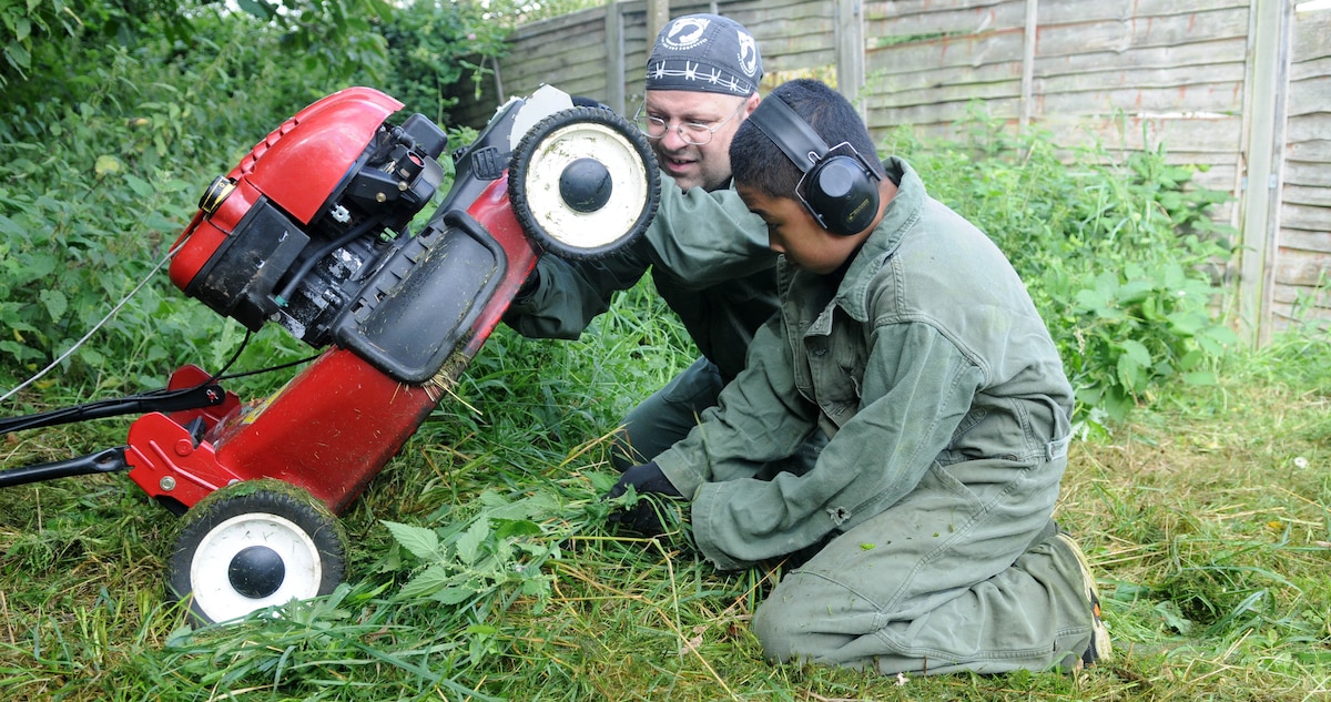 BECK ROW, England – Master Sgt. Eric Leirer, 352nd Special Operations Maintenance Squadron, and his 13-year-old son Albert Valen, remove tangled grass from their lawn mower after mowing a huge area of overgrowth in the backyard of a disabled resident in Beck Row, a community just outside RAF Mildenhall, Aug. 25, 2012. Leirer and other volunteers, including his 13-year-old son, took on the task of clearing the yard for the homeowner, who was unable to perform the task herself. (U.S. Air Force photo/Staff Sgt. Austin M. May)