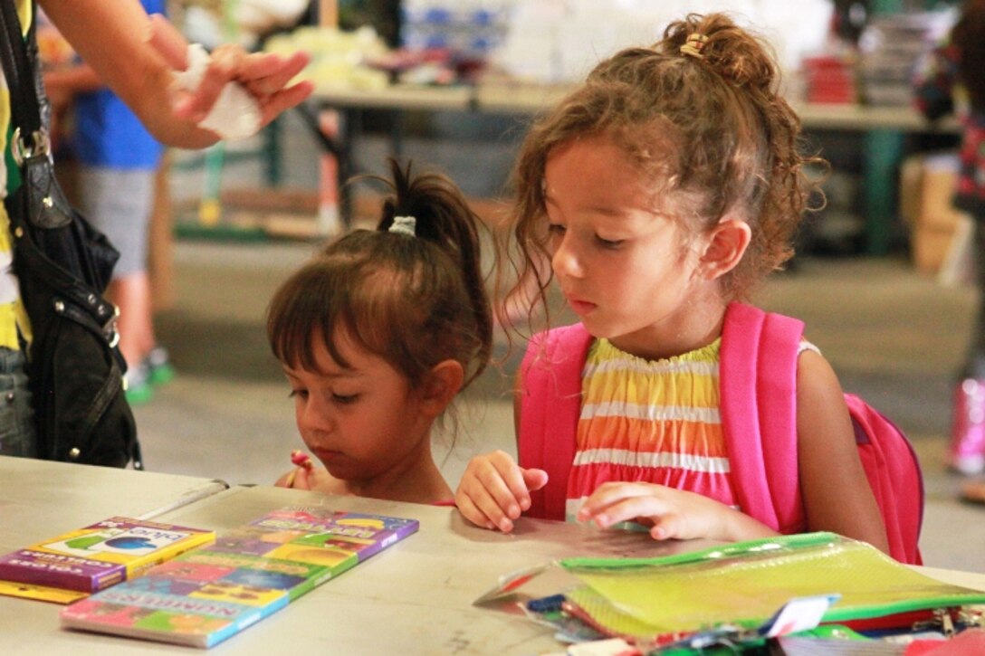 Bella Walters (right), 5, and her sister, Annika (left), 3, gather school supplies during a school supply give-away at Camp Pendleton, Calif., Aug. 6. A group of family readiness officers with 1st Marine Logistics Group and Marine Corps Community Services coordinated the give-away with a variety of donated supplies for children of all school grades. More than 100 families registered to receive the school supplies.