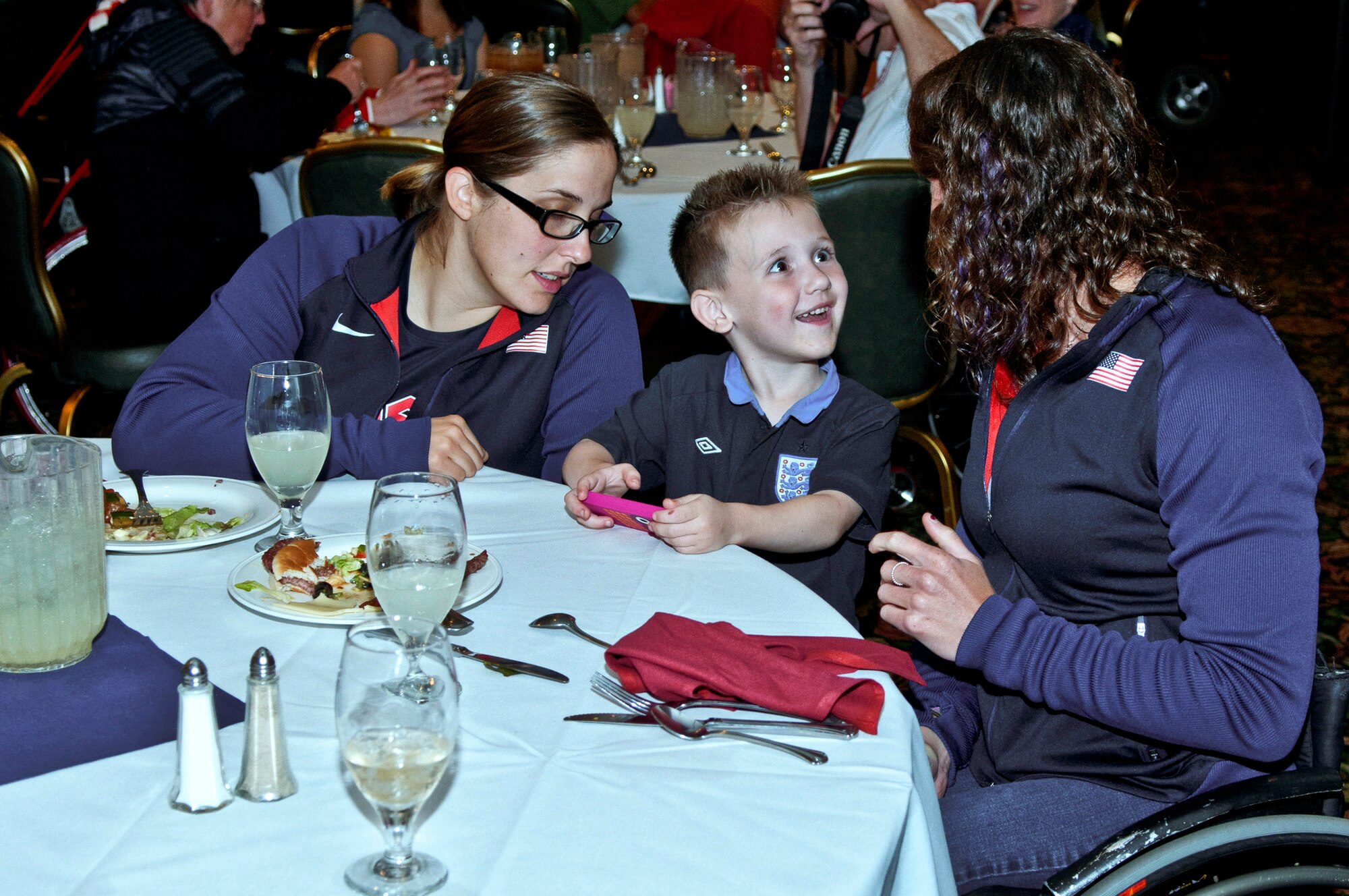 ROYAL AIR FORCE LAKENHEATH, England - Joshua Sonustun, age 4, interacts with U.S. Paralympians, Christina Schwab (left) and Tatyana McFadden (right), during the Paralympics Sponsor Family dinner at Eagles Landing Aug. 23, 2012. The purpose of the dinner was to thank the sponsors for hosting the athletes in their homes.  More than 50 U.S. Paralympians and hopefuls honed their skills and made final preparations here Aug. 18 through 25 for competition in the London 2012 Paralympic Games. (U.S. Air Force photo by Senior Airman Connor Estes)