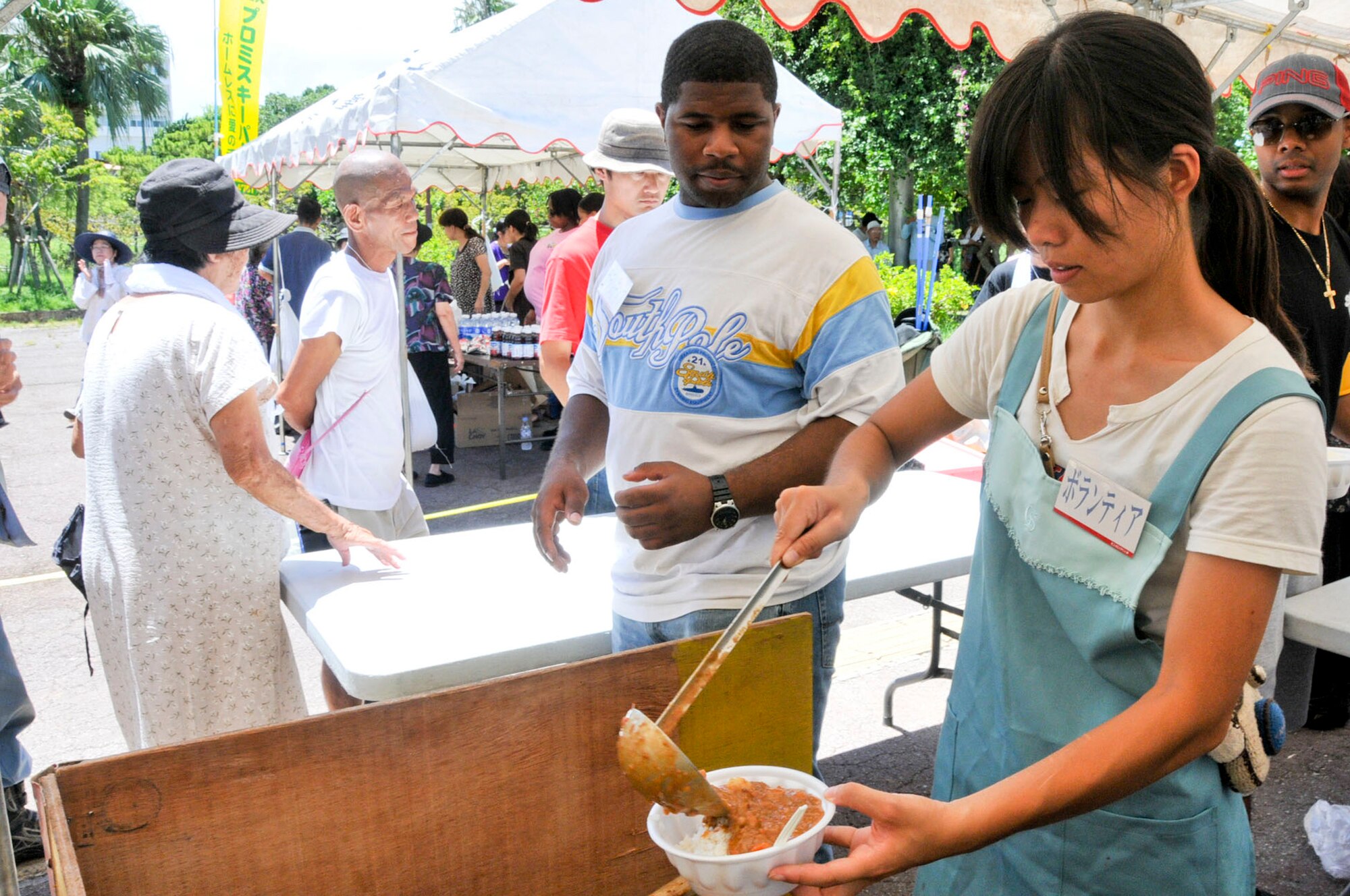 Rio Kakinohama, local volunteer, pours a bowl of curry to hand to U.S. Air Force Tech. Sgt. James Parks, Kadena 5/6 Club member, during a volunteer event to feed the homeless in Yogi Park in Naha on Aug. 18, 2012. The volunteers served more than 200 less fortunate people in an hour. The 5/6 Club donated sandwich platters and cases of water to support this event. (U.S. Air Force photo/Staff Sgt. Darnell T. Cannady)